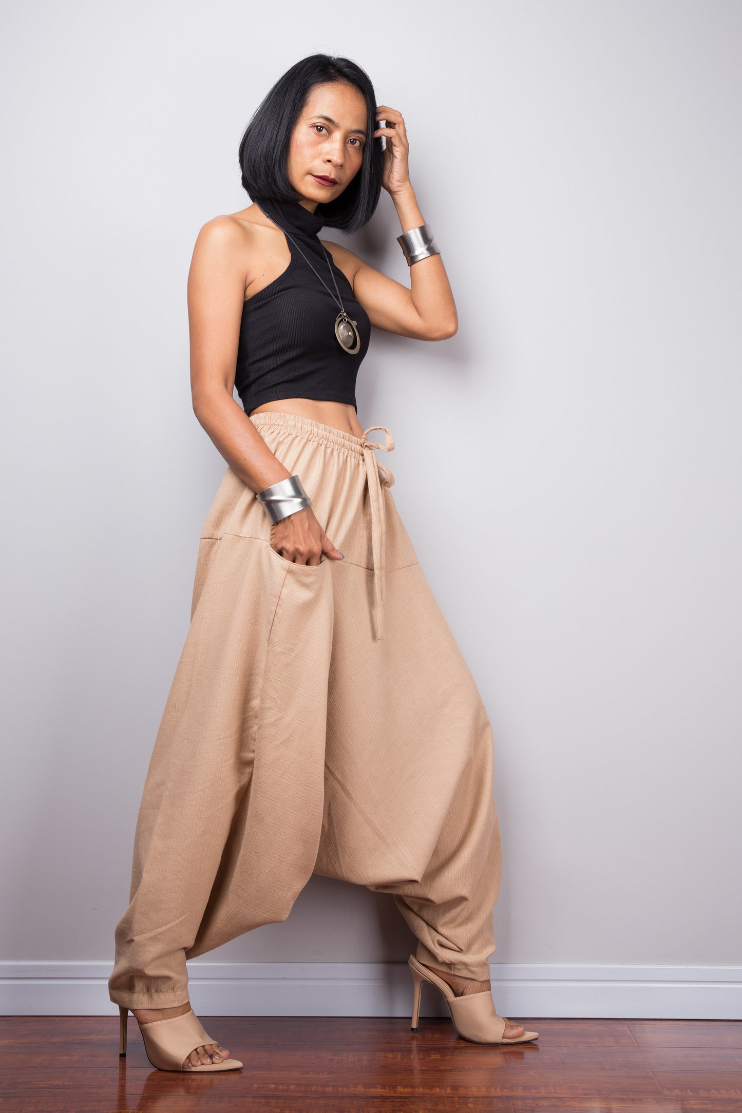 Side view of the beige cotton harem pants, displaying the loose fit and the flow of the fabric from the waist to the hem.