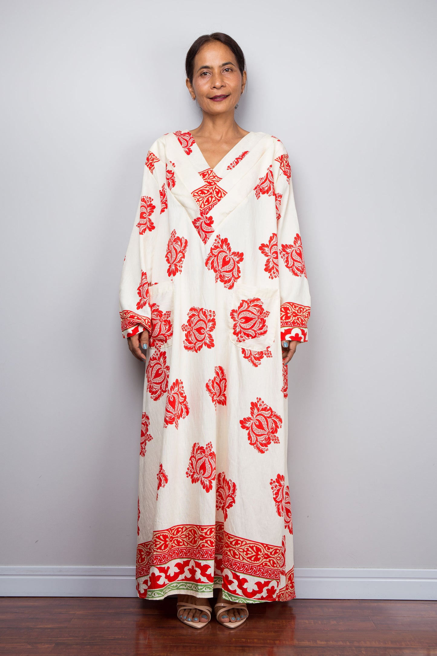 Woman wearing a long, white dress with red floral patterns against a plain background