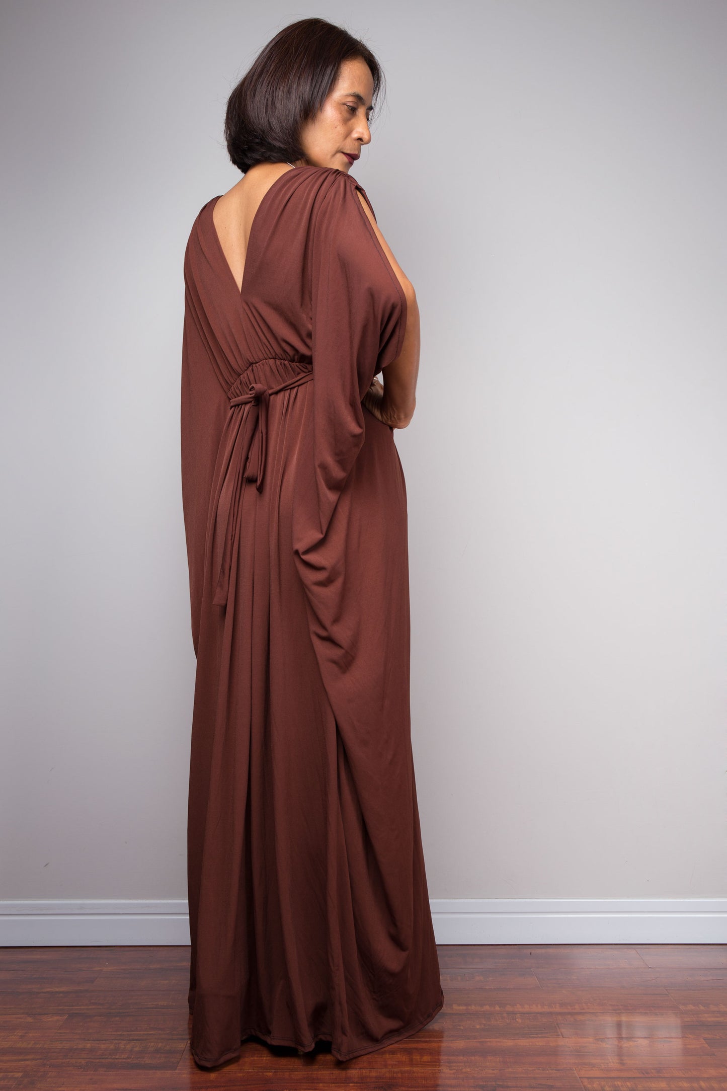 Woman wearing a brown evening caftan gown against a plain wall.