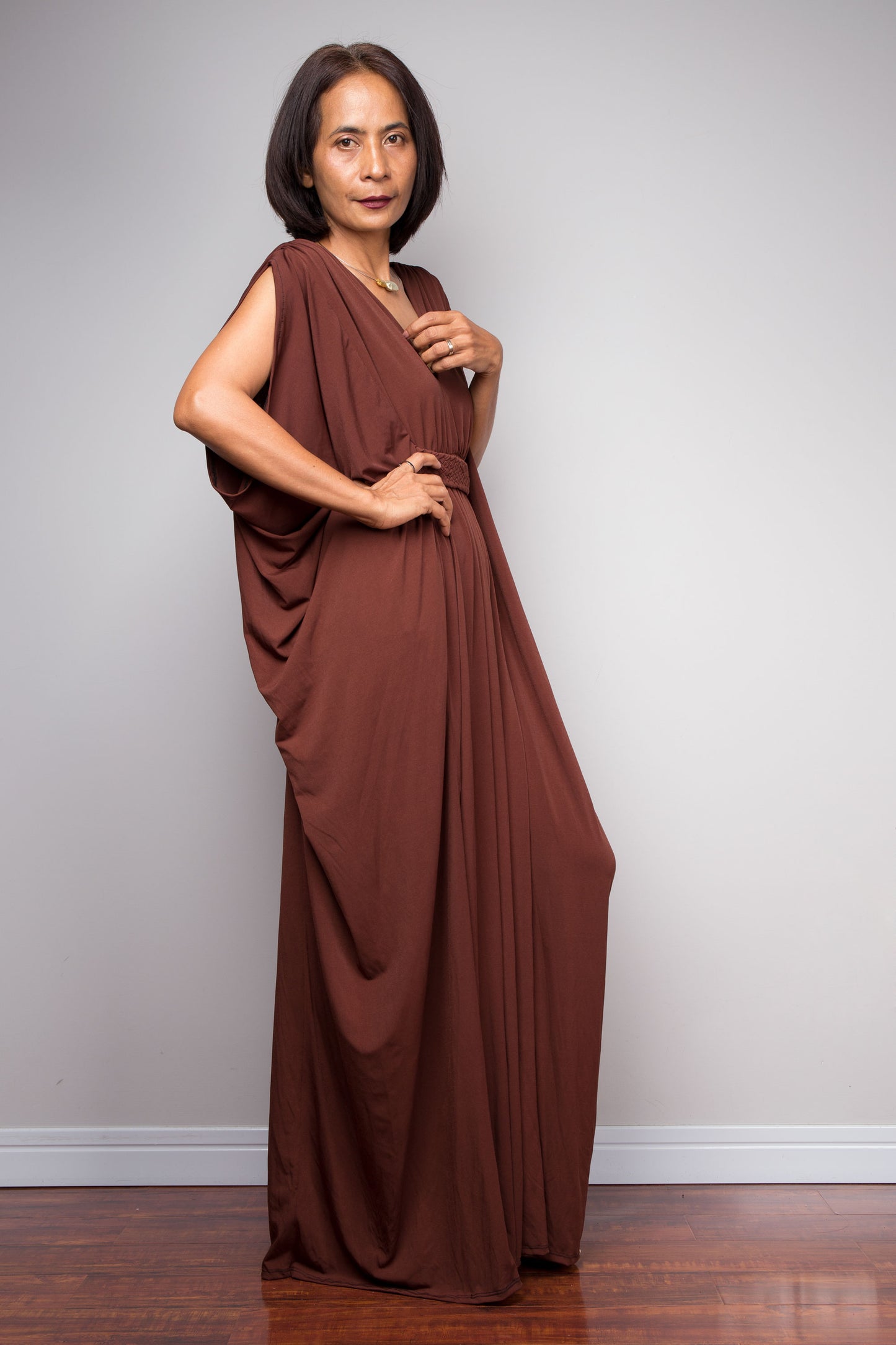 Woman wearing a brown draped caftan dress by Nuichan against a plain background