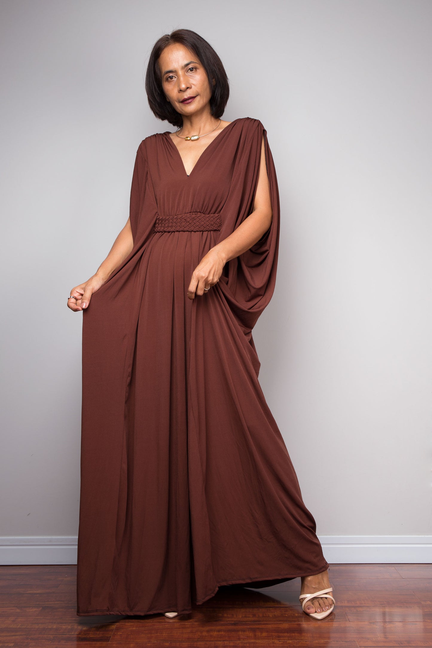 Woman wearing a brown draped dress by Nuichan against a plain background