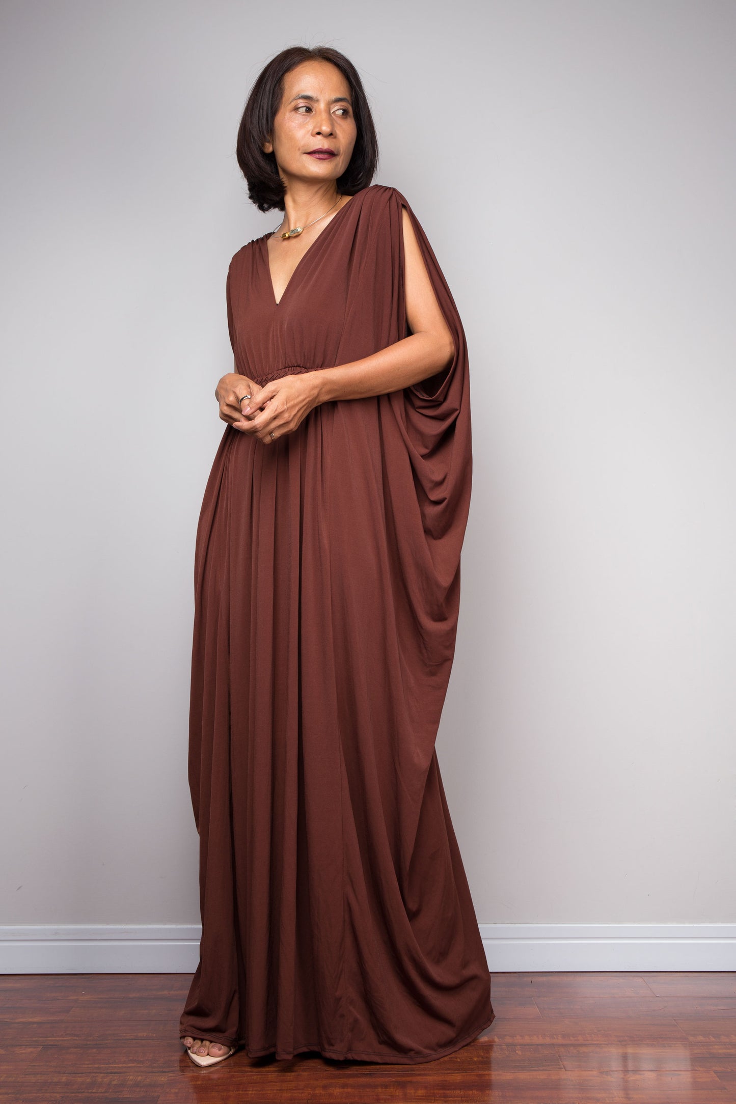 Woman wearing a brown draped caftan dress against a plain background
