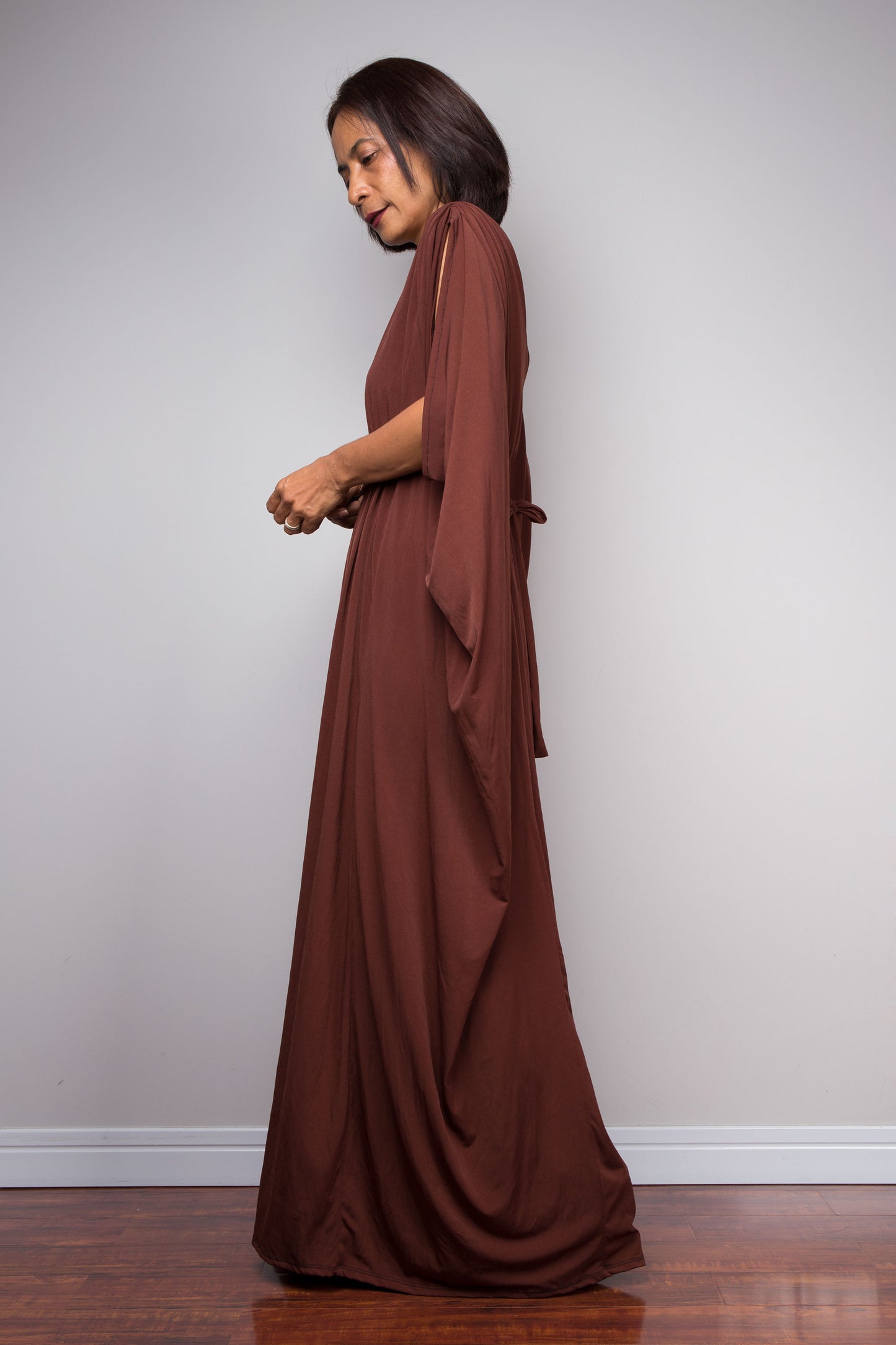 Woman wearing a long brown caftan dress against a plain background