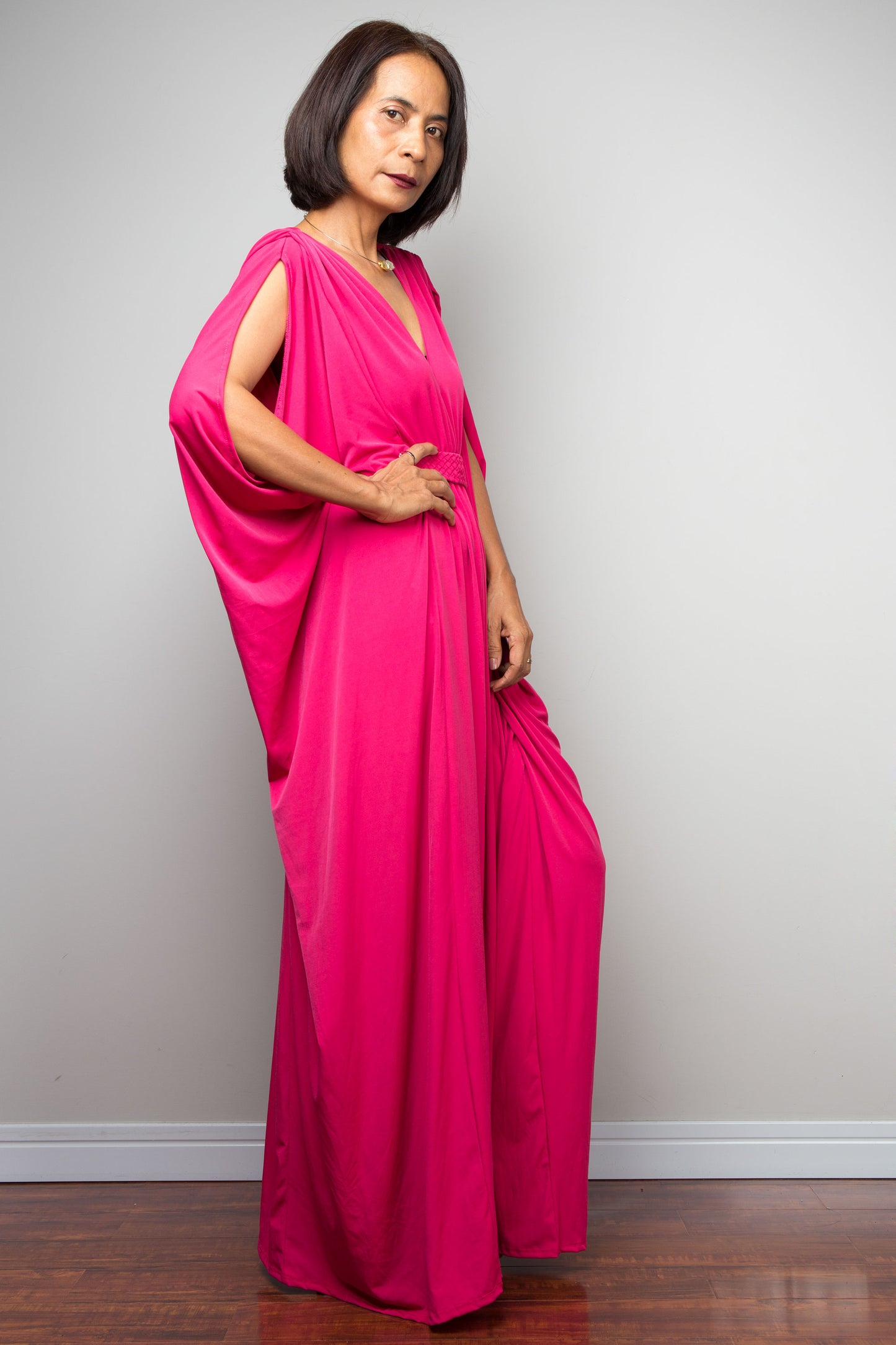Petite woman wearing a bright pink maxi dress against a plain background