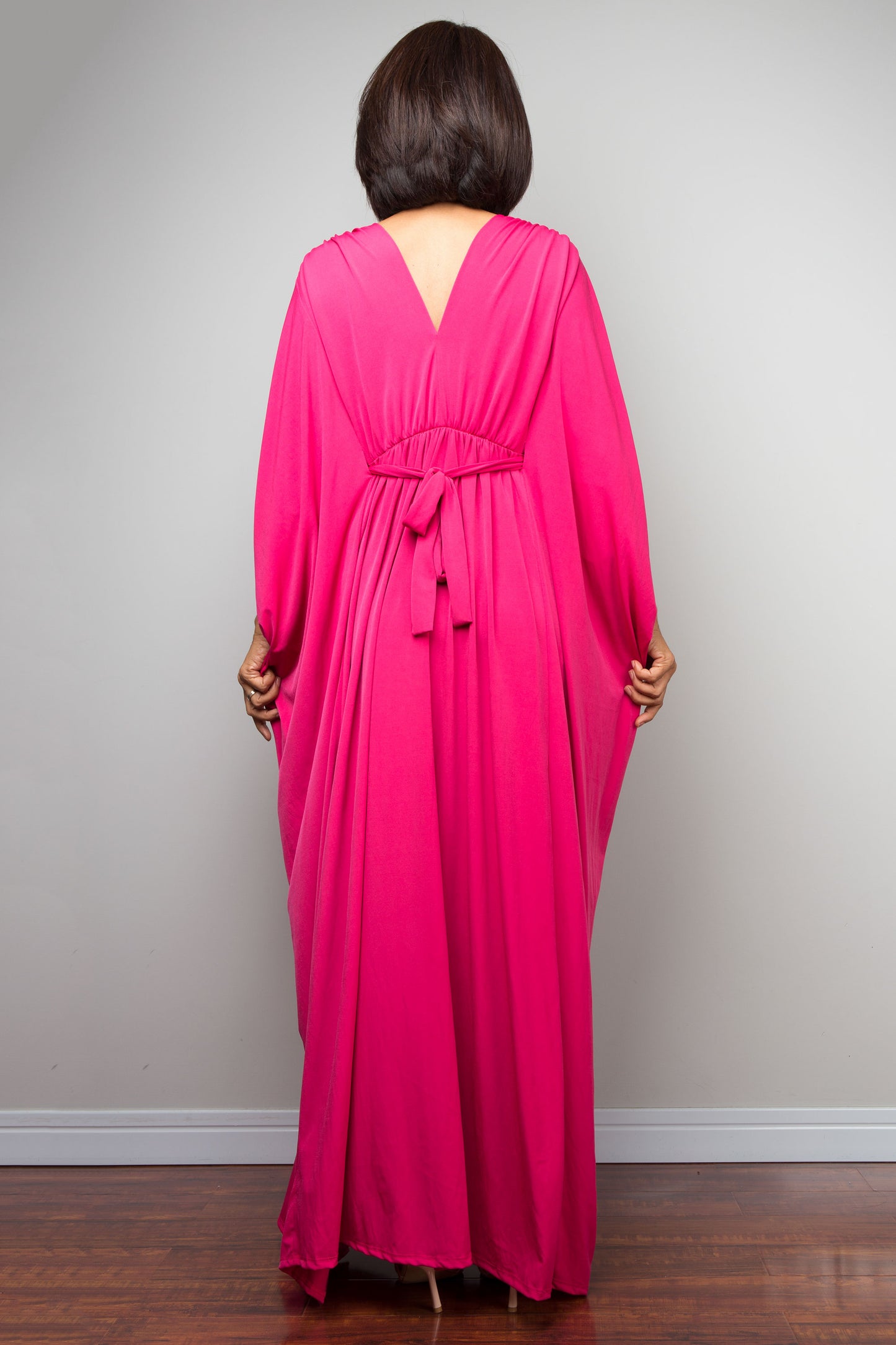 Petite woman wearing a bright pink caftan dress with a deep neckline and long sleeves against a plain background.
