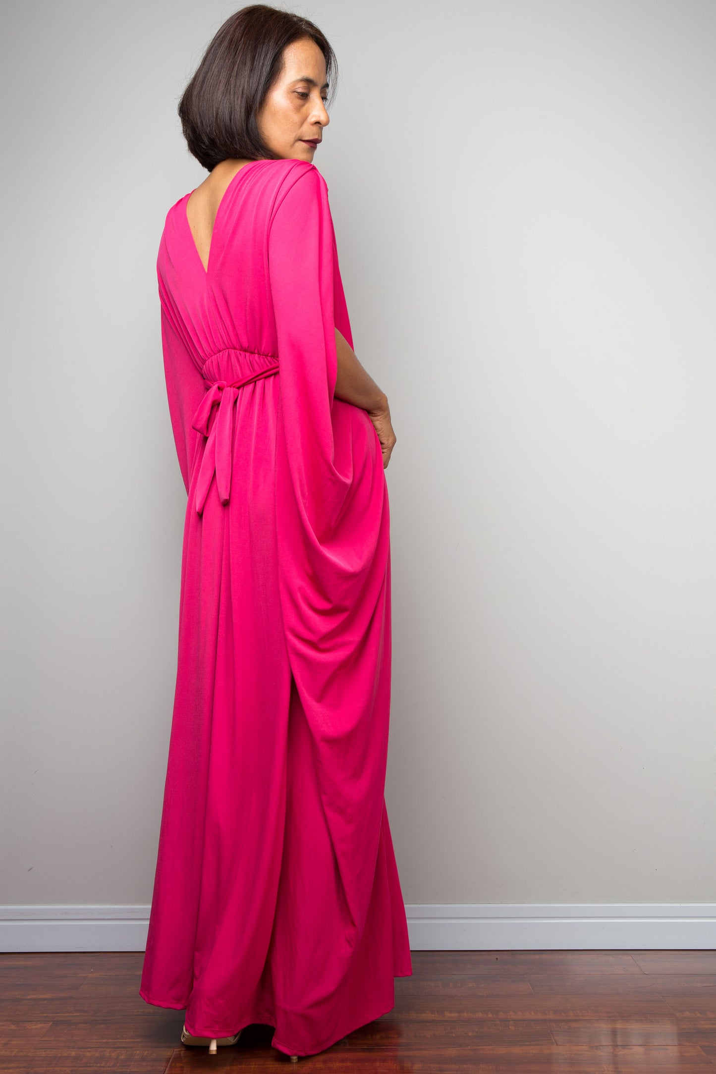 Petite woman wearing a bright pink kaftan against a plain background