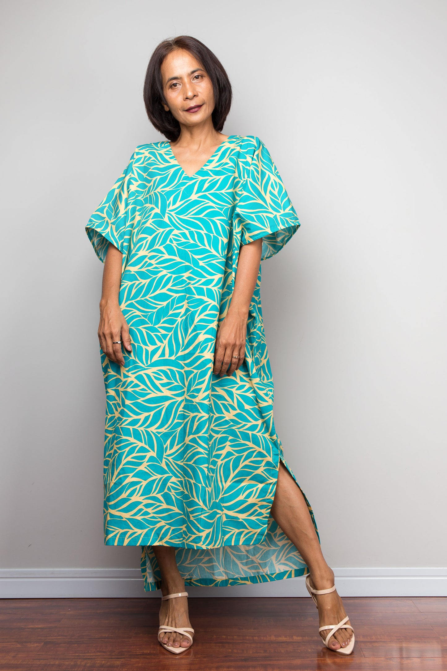 Woman wearing an aqua cotton caftan dress with leaf pattern against a plain background