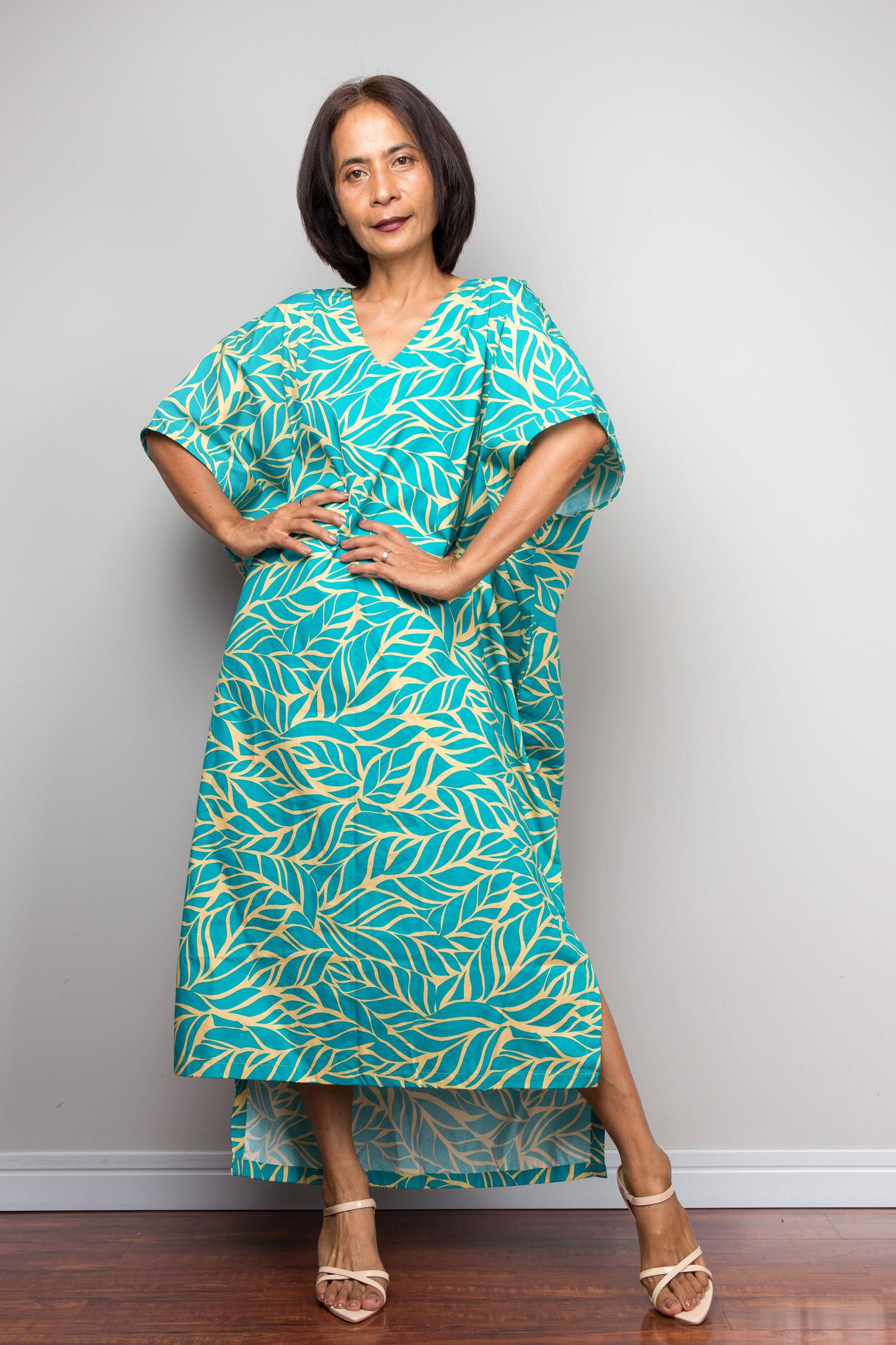 Woman wearing an aqua cotton caftan dress with yellow leaf pattern against a plain background