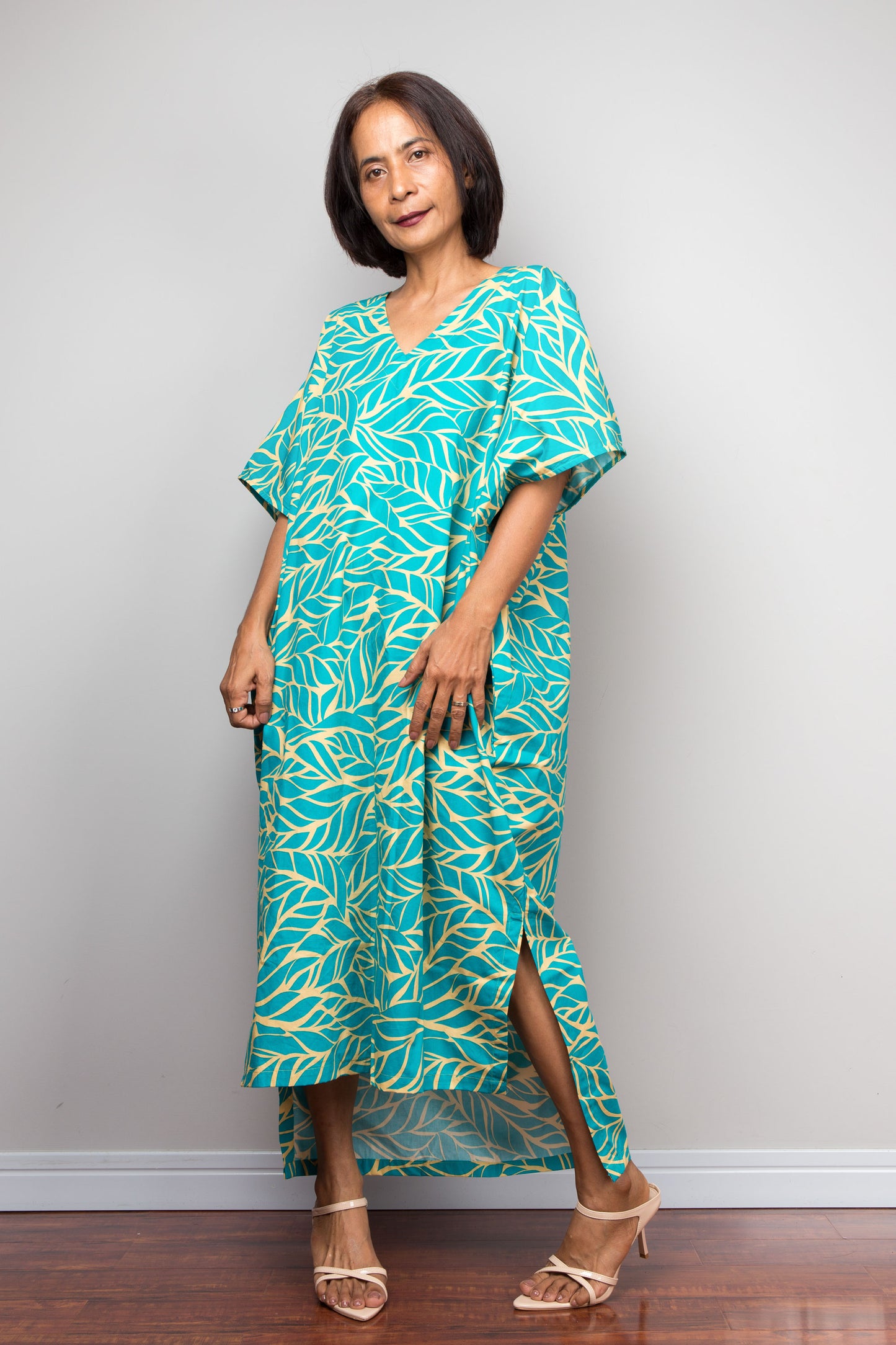 Petite woman wearing an aqua green and yellow patterned cotton caftan dress against a plain background