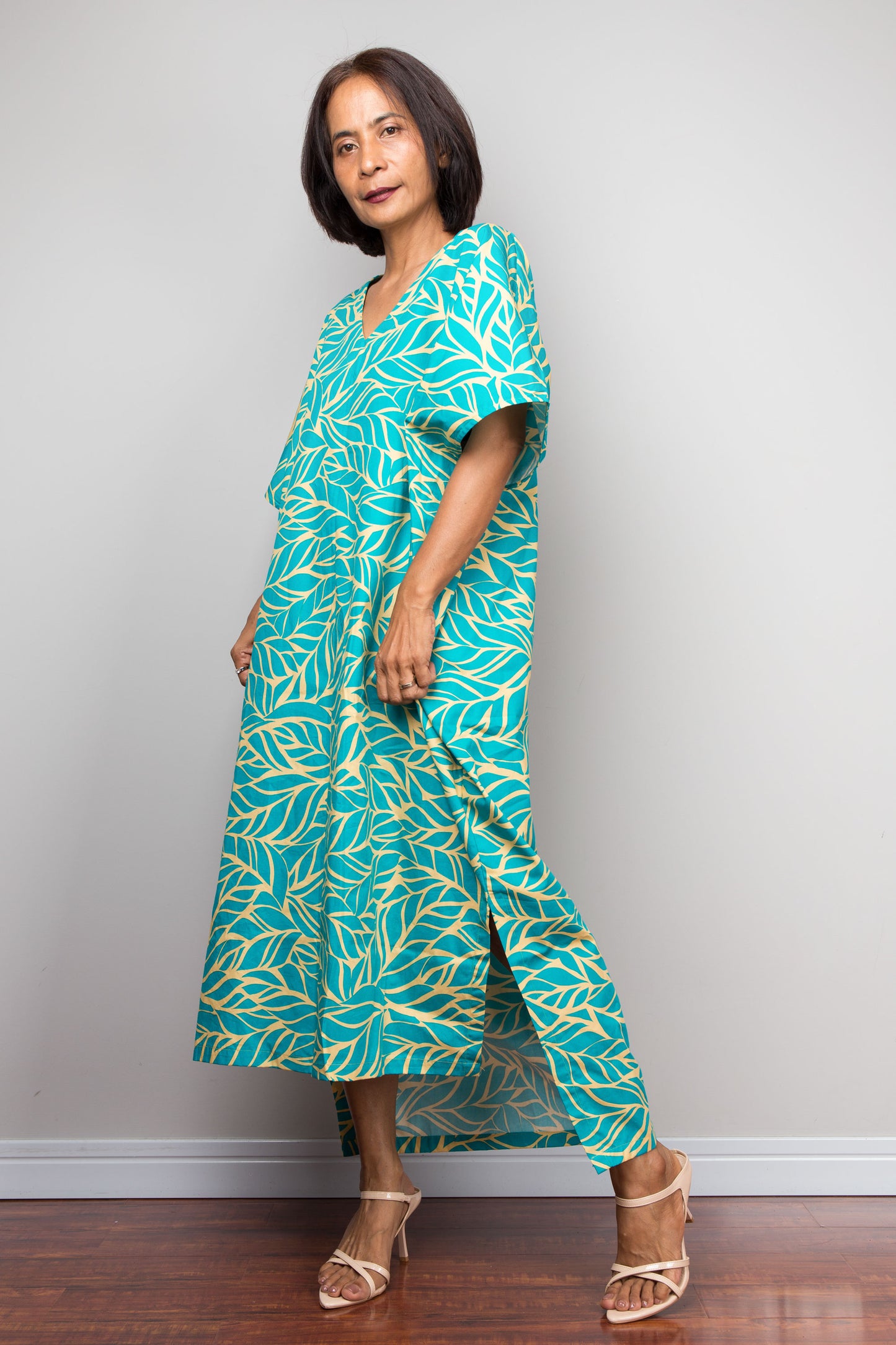 Woman wearing a teal and yellow patterned cotton caftan petite dress against a plain background