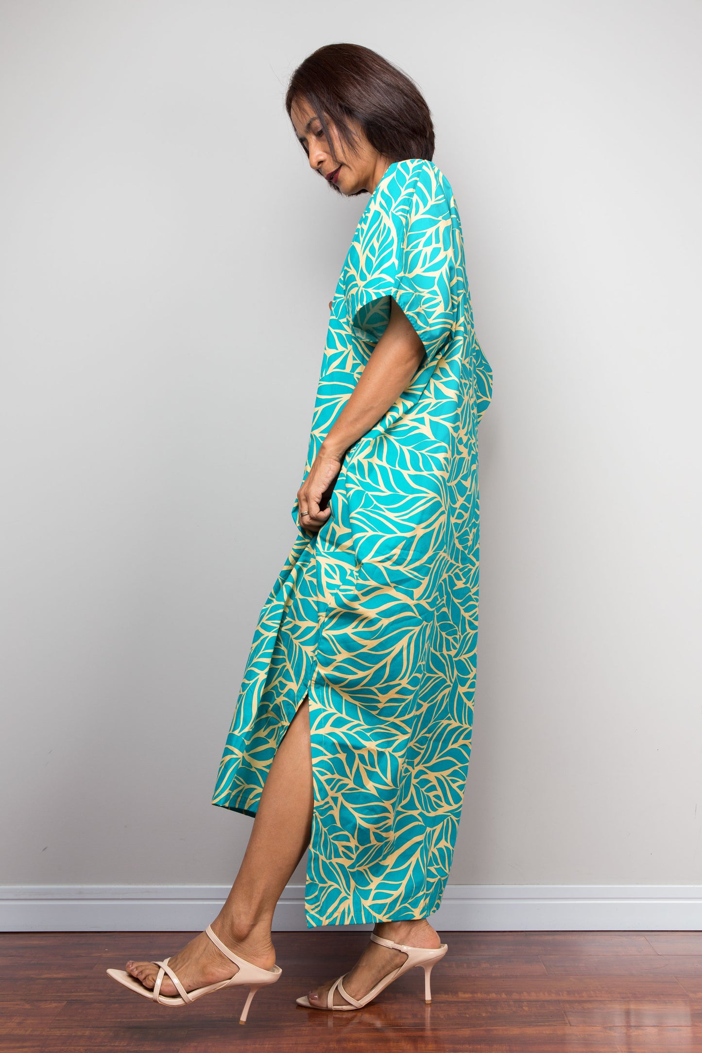 Woman wearing an aqua green and yellow patterned cotton kaftan dress for petite against a plain background