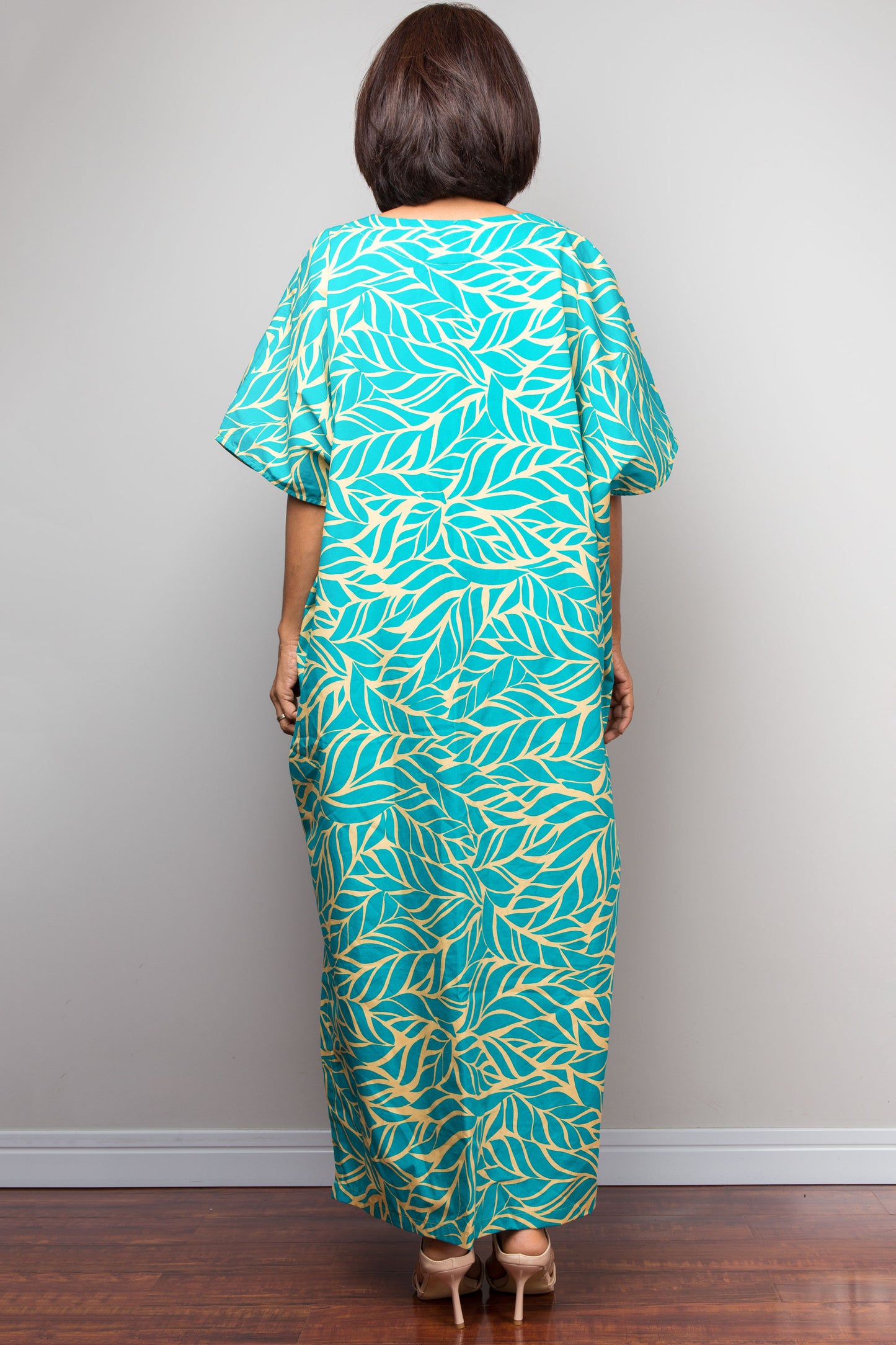 Petite woman wearing an aqua green and yellow patterned kaftan dress against a plain background