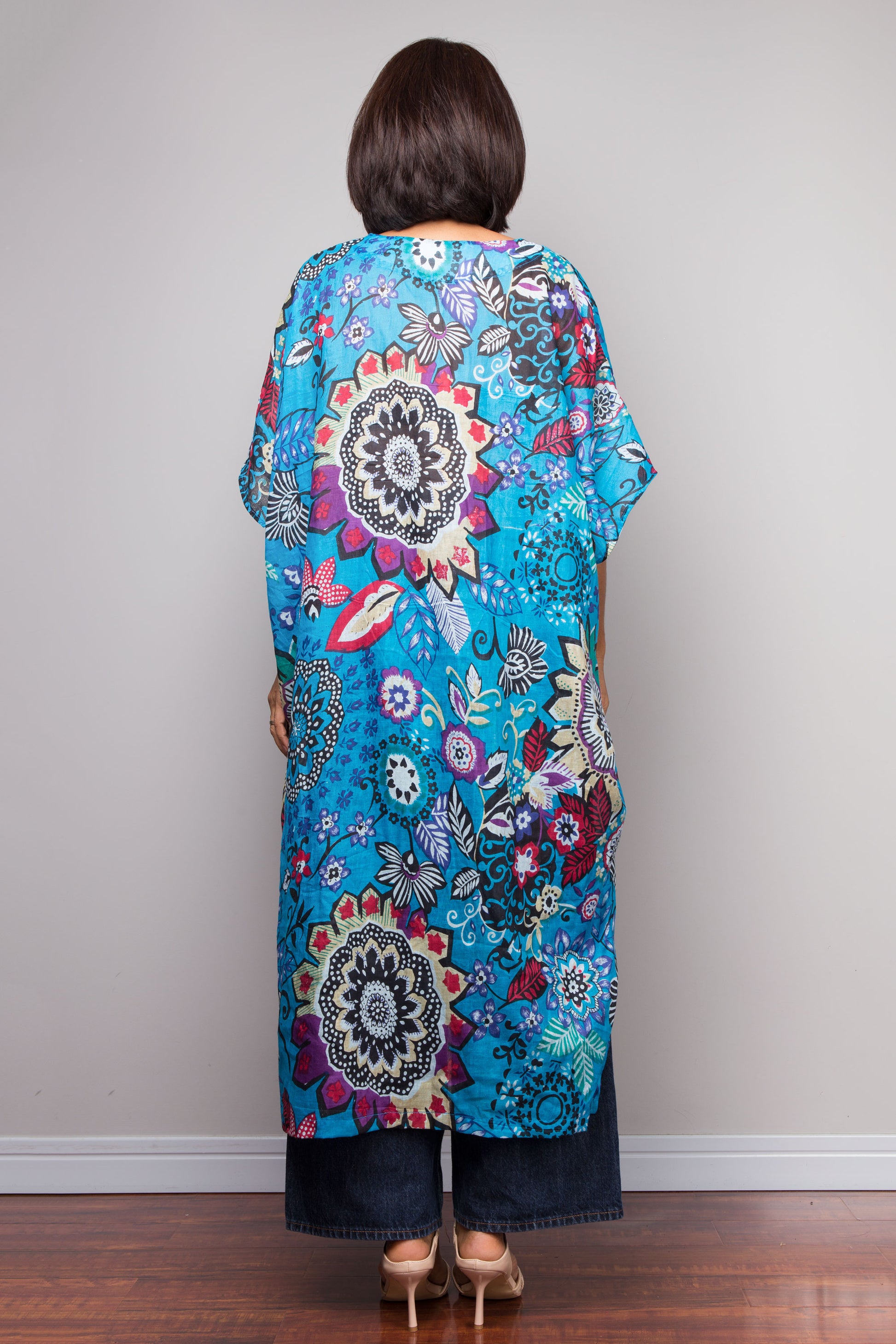 Woman wearing a colorful floral and mandala patterned dress against a plain background