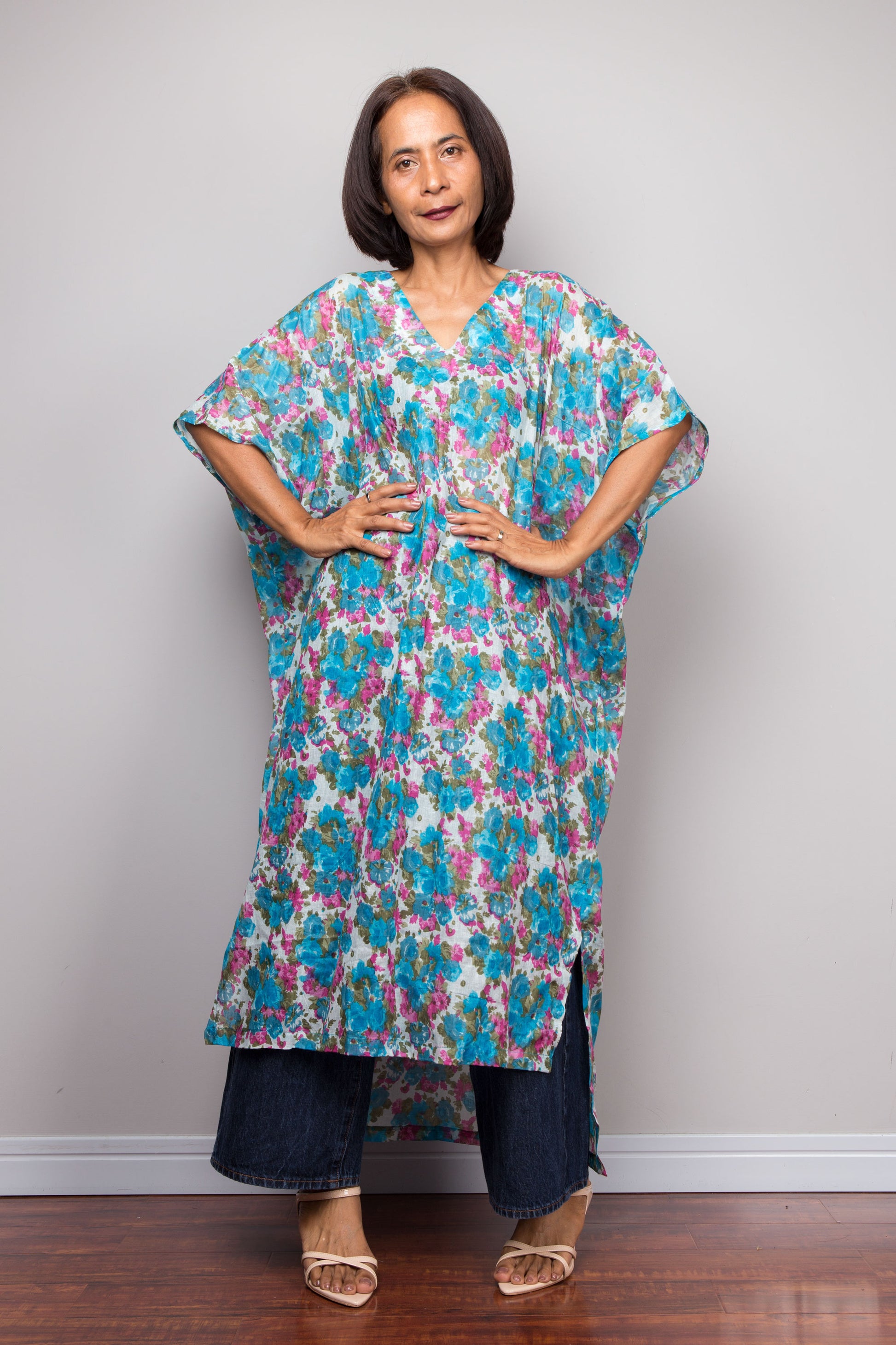 Woman wearing a colorful floral cotton caftan dress against a plain background
