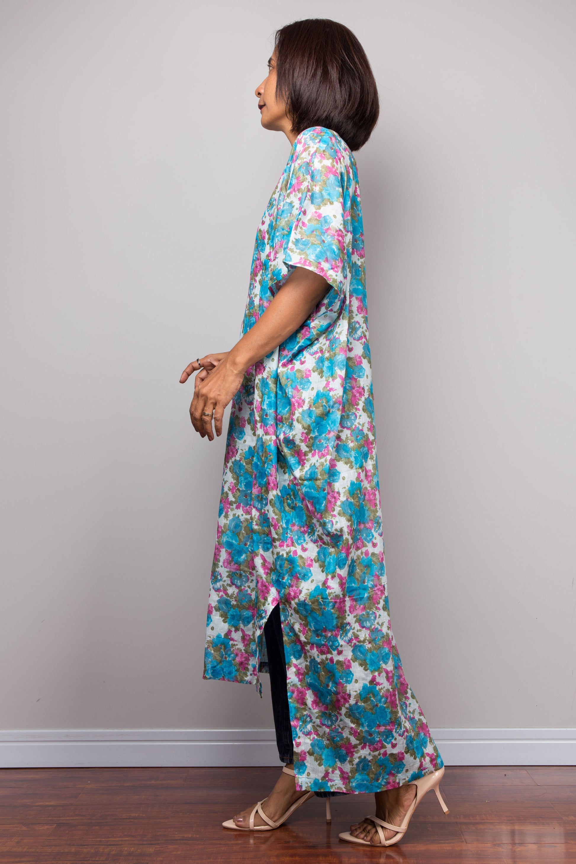 Woman wearing a floral dress standing against a plain wall.