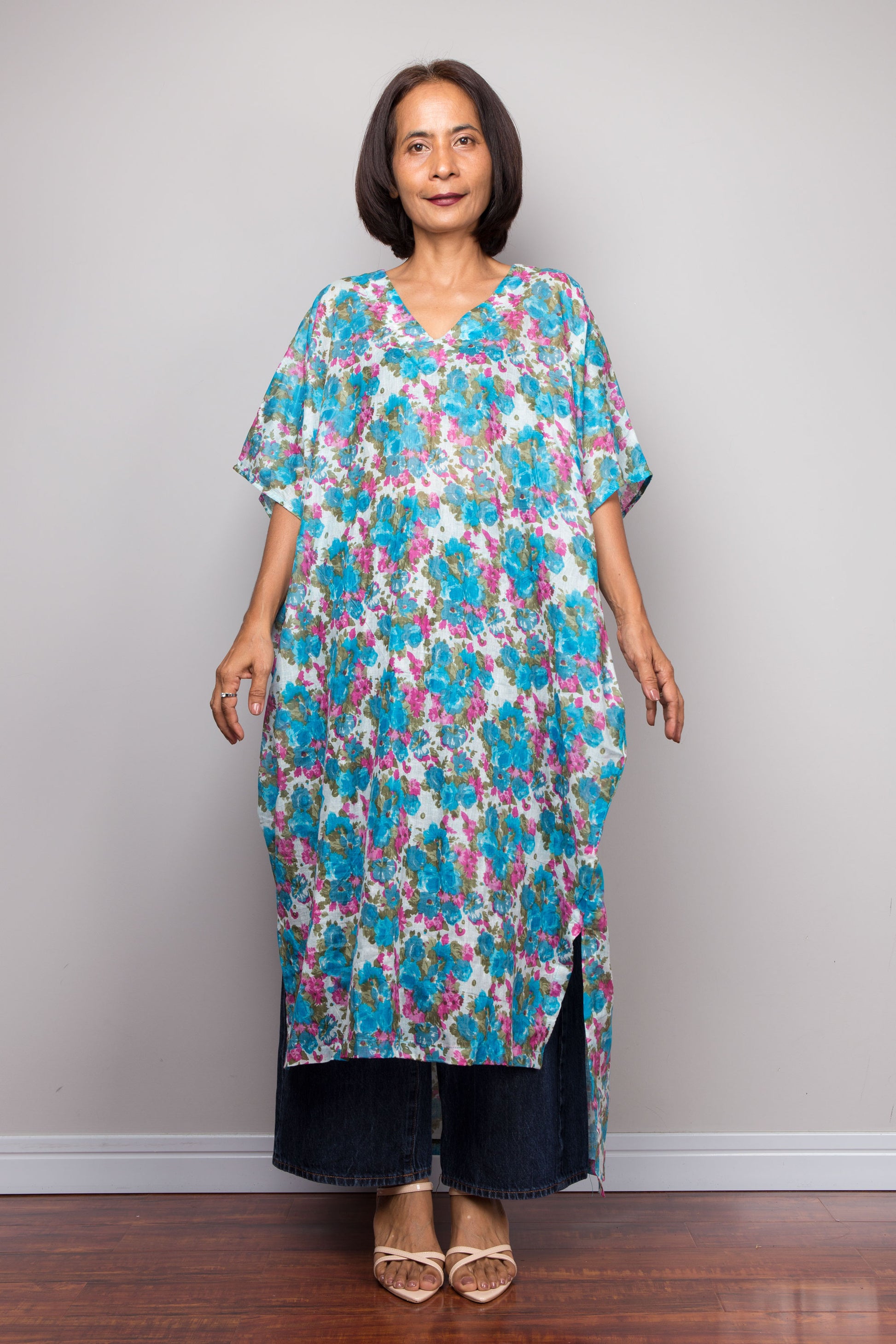 Woman wearing a colorful floral caftan midi dress against a plain background