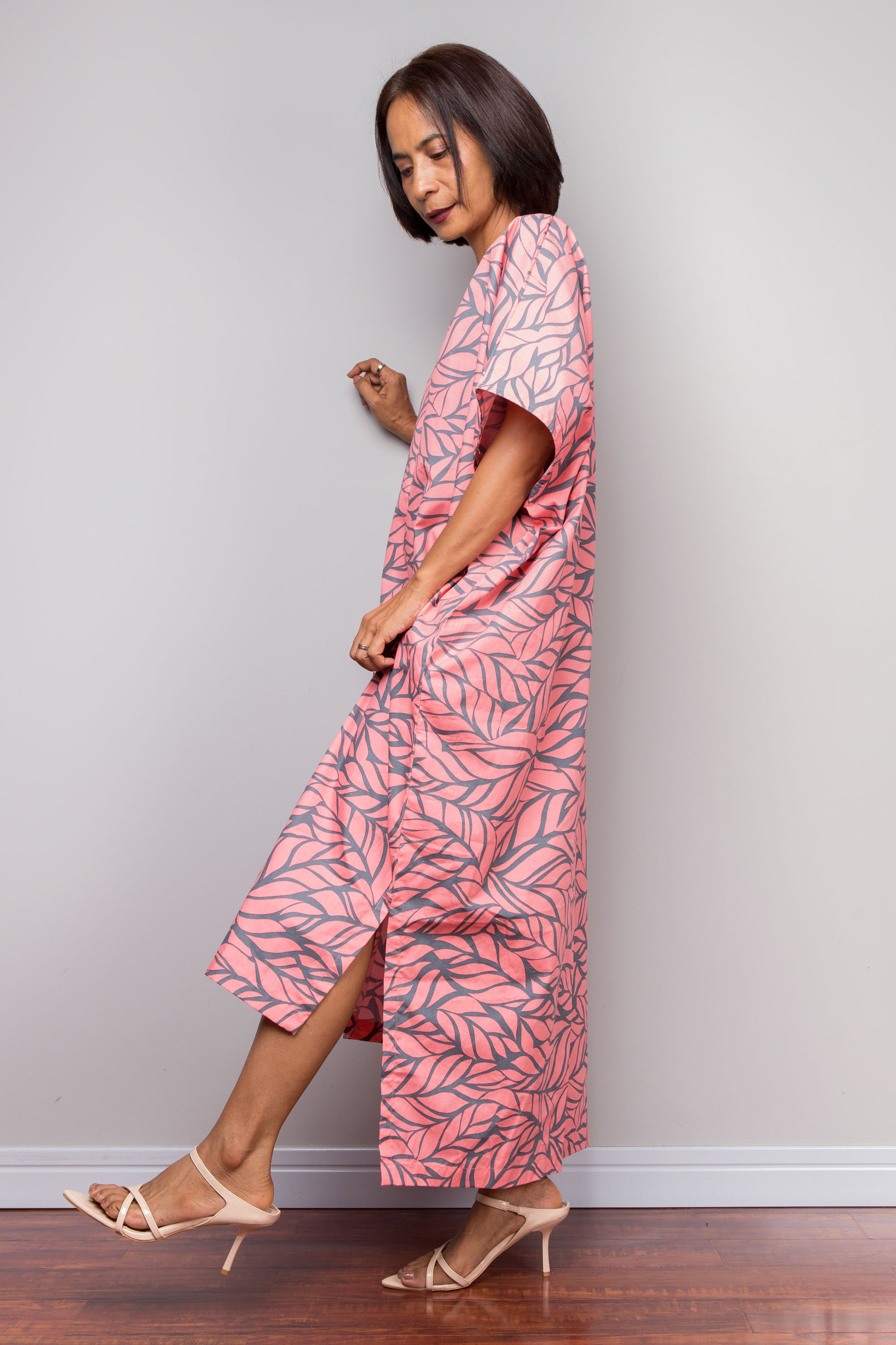 Woman wearing a pink leaf-patterned kaftan dress against a plain background
