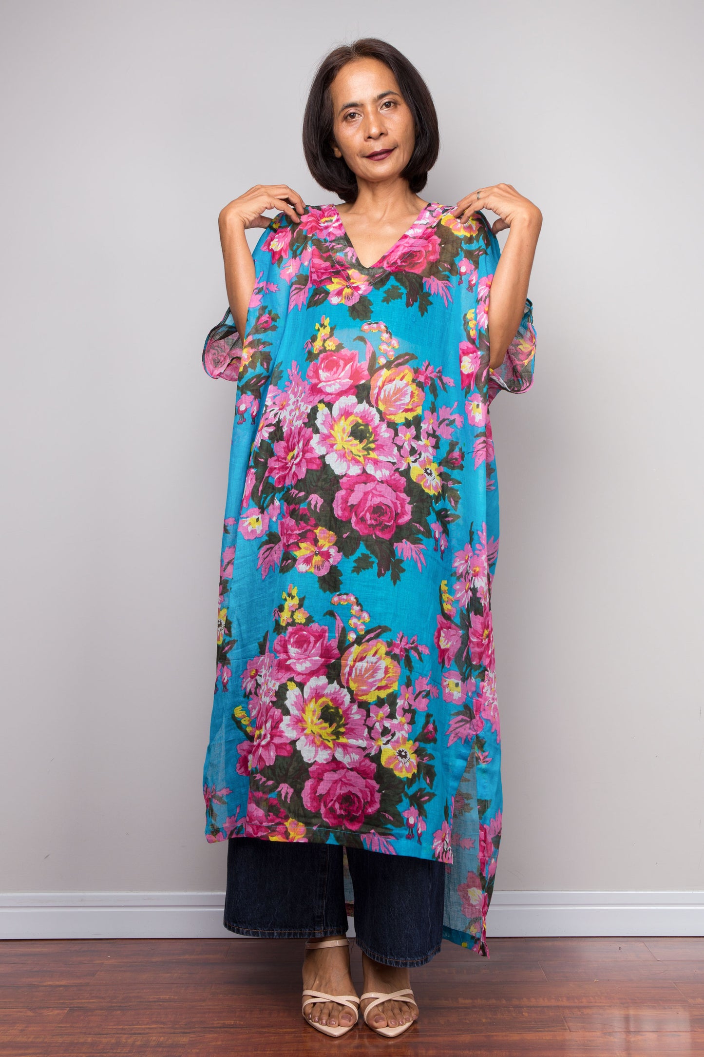 Woman wearing a colorful floral kaftan midi dress against a plain background