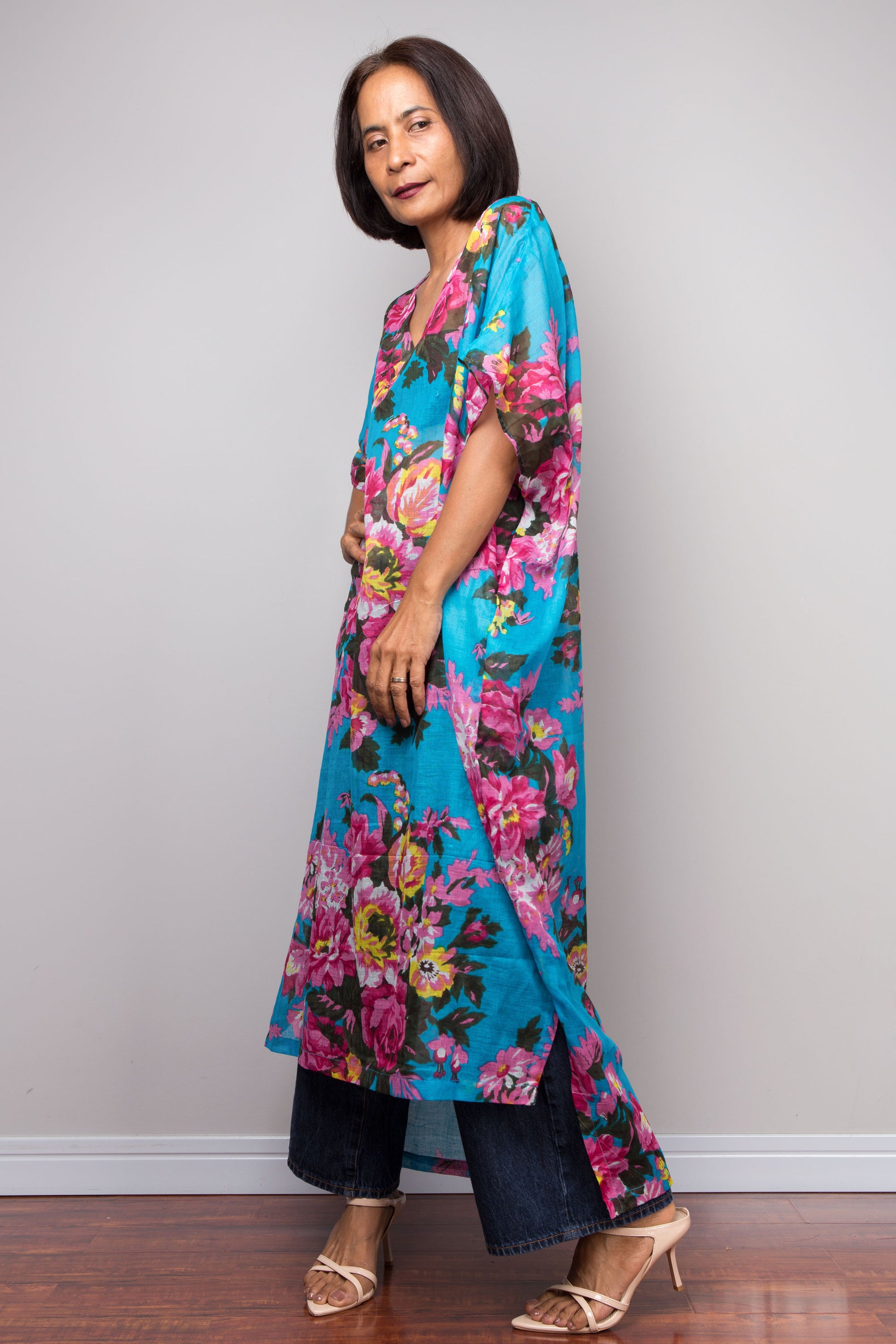 Woman wearing a colorful floral kaftan maxi dress against a plain background
