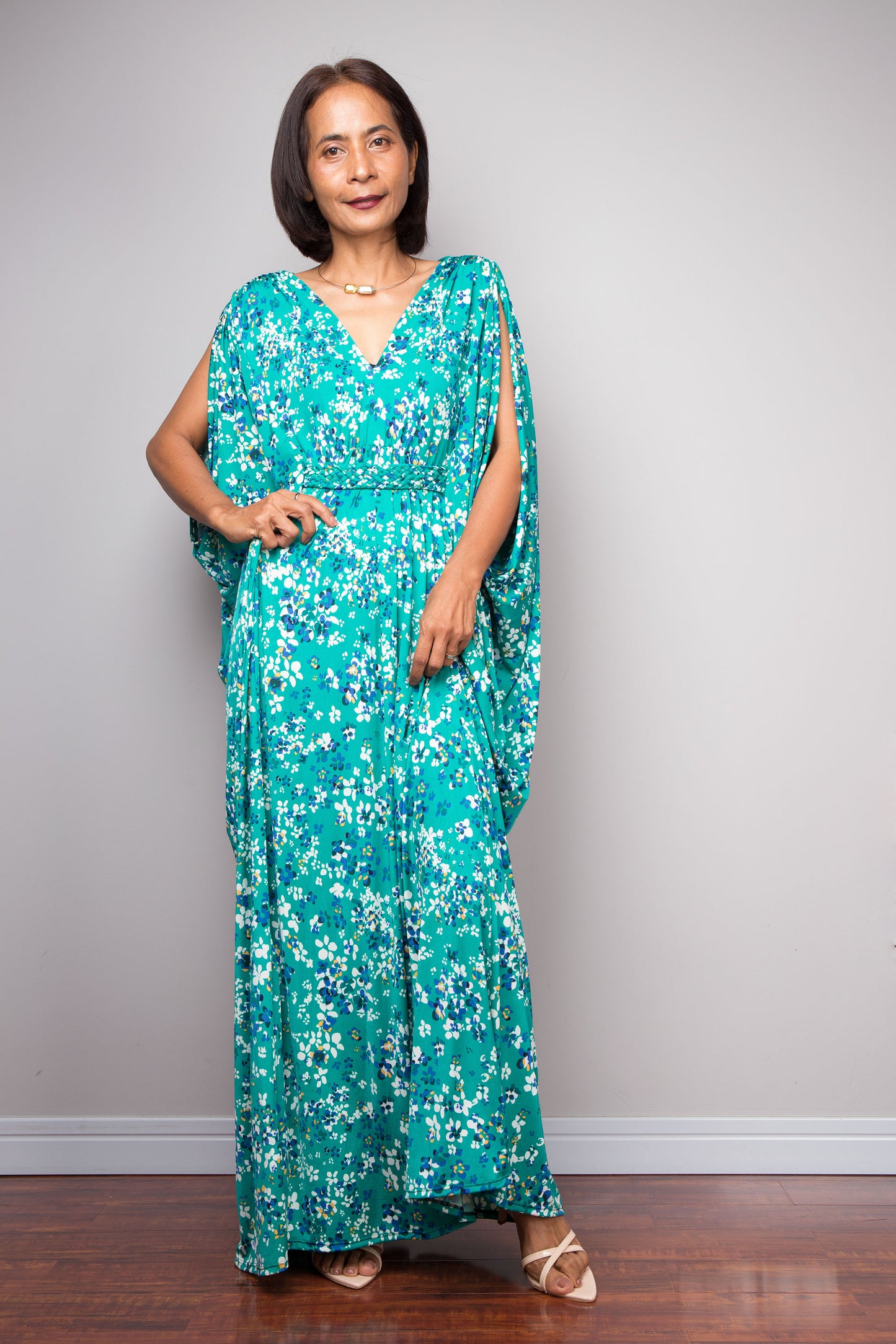 Woman wearing a teal green floral caftan maxi dress against a plain background