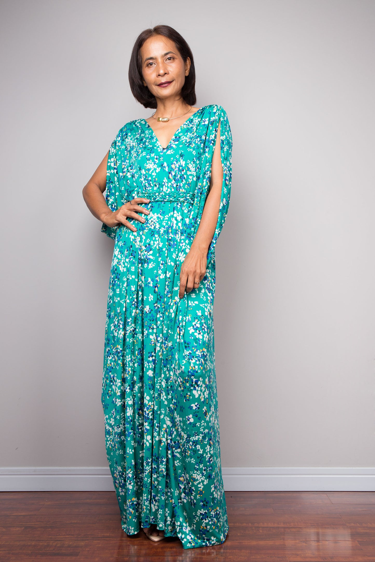 Woman wearing a teal green floral caftan dress against a plain background