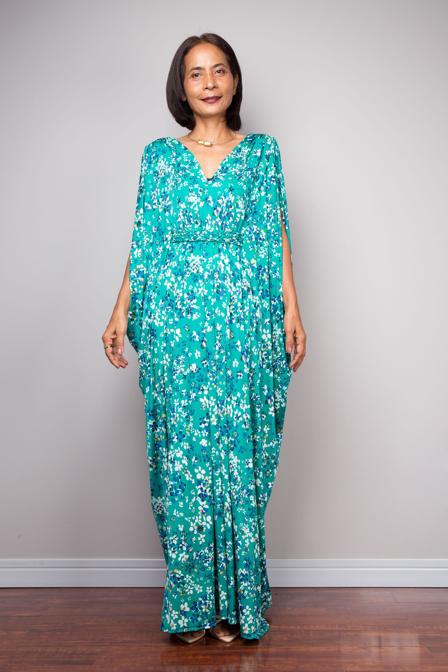 Petite woman wearing a teal green floral caftan dress against a plain background