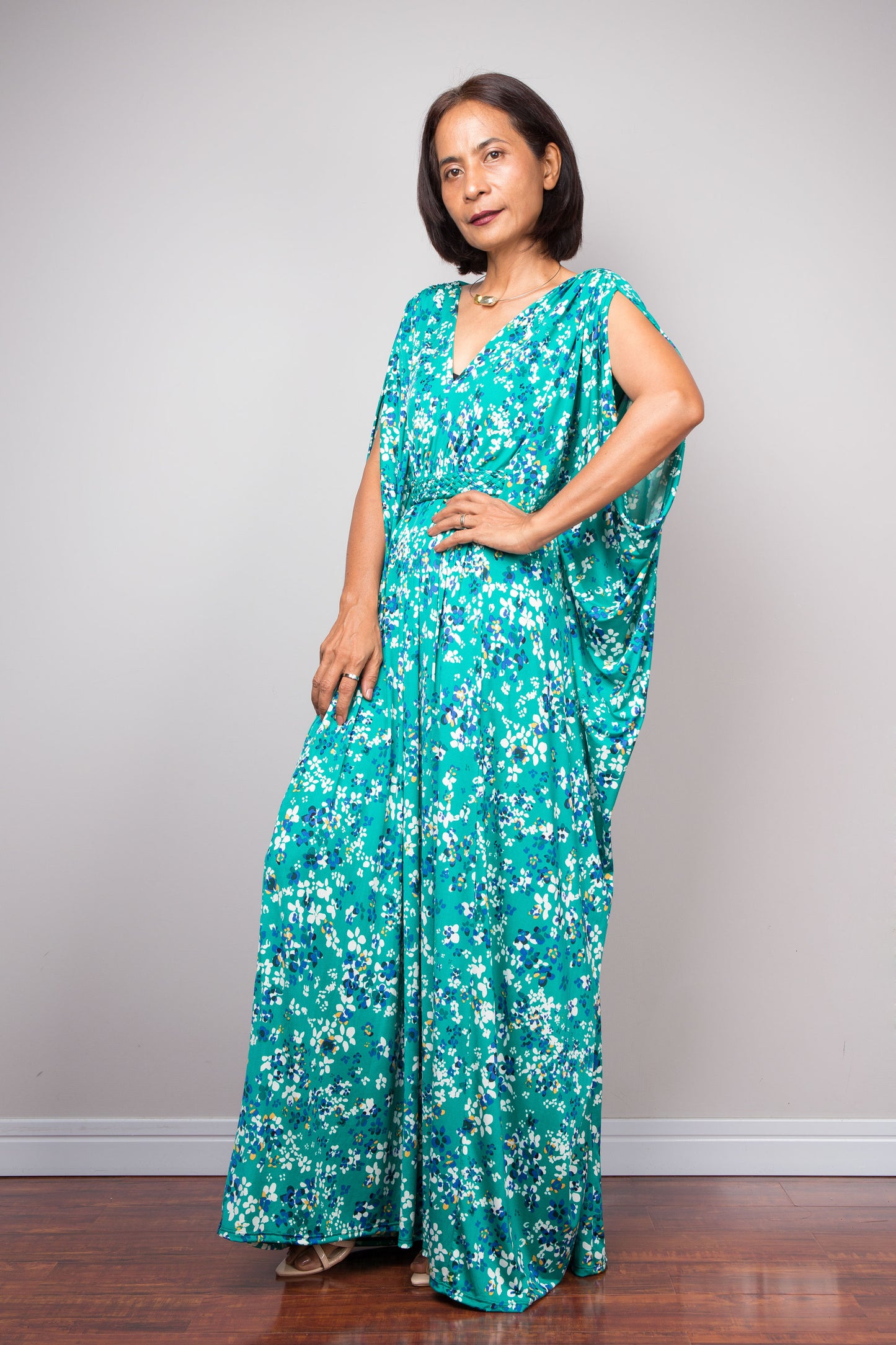 Petite woman wearing a teal green floral caftan against a plain background