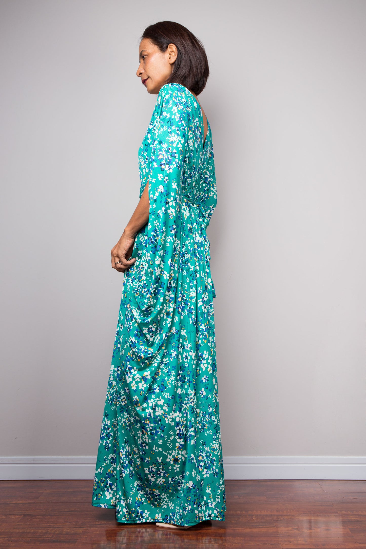 Woman wearing a teal green floral petite caftan dress against a plain background