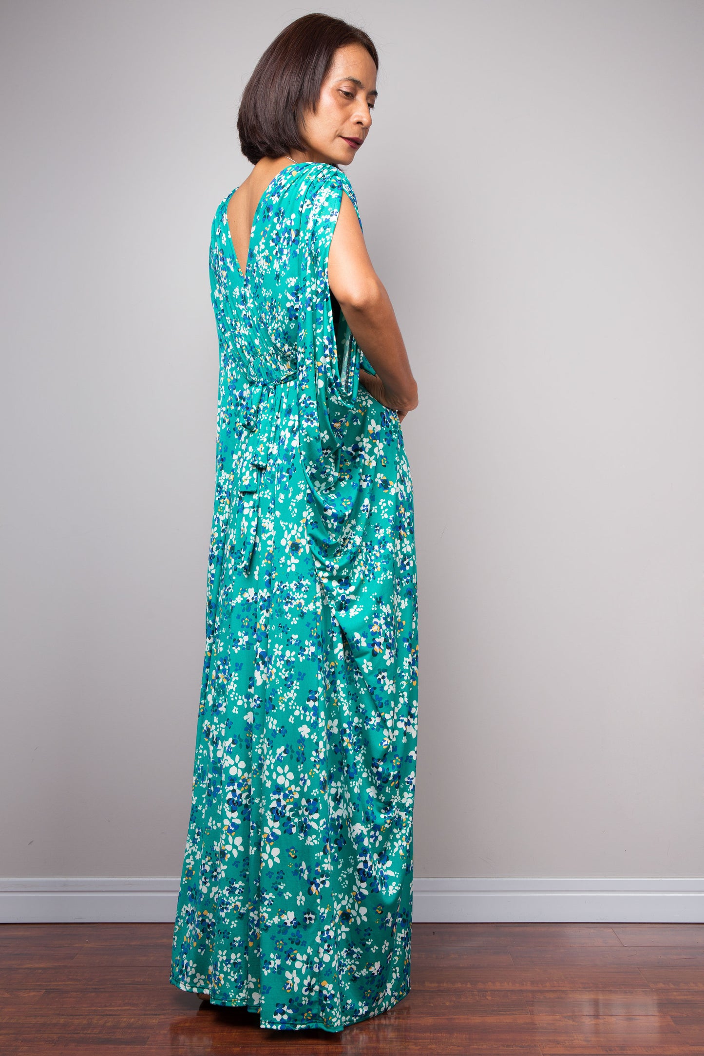 Woman wearing a long teal green floral caftan dress against a plain background