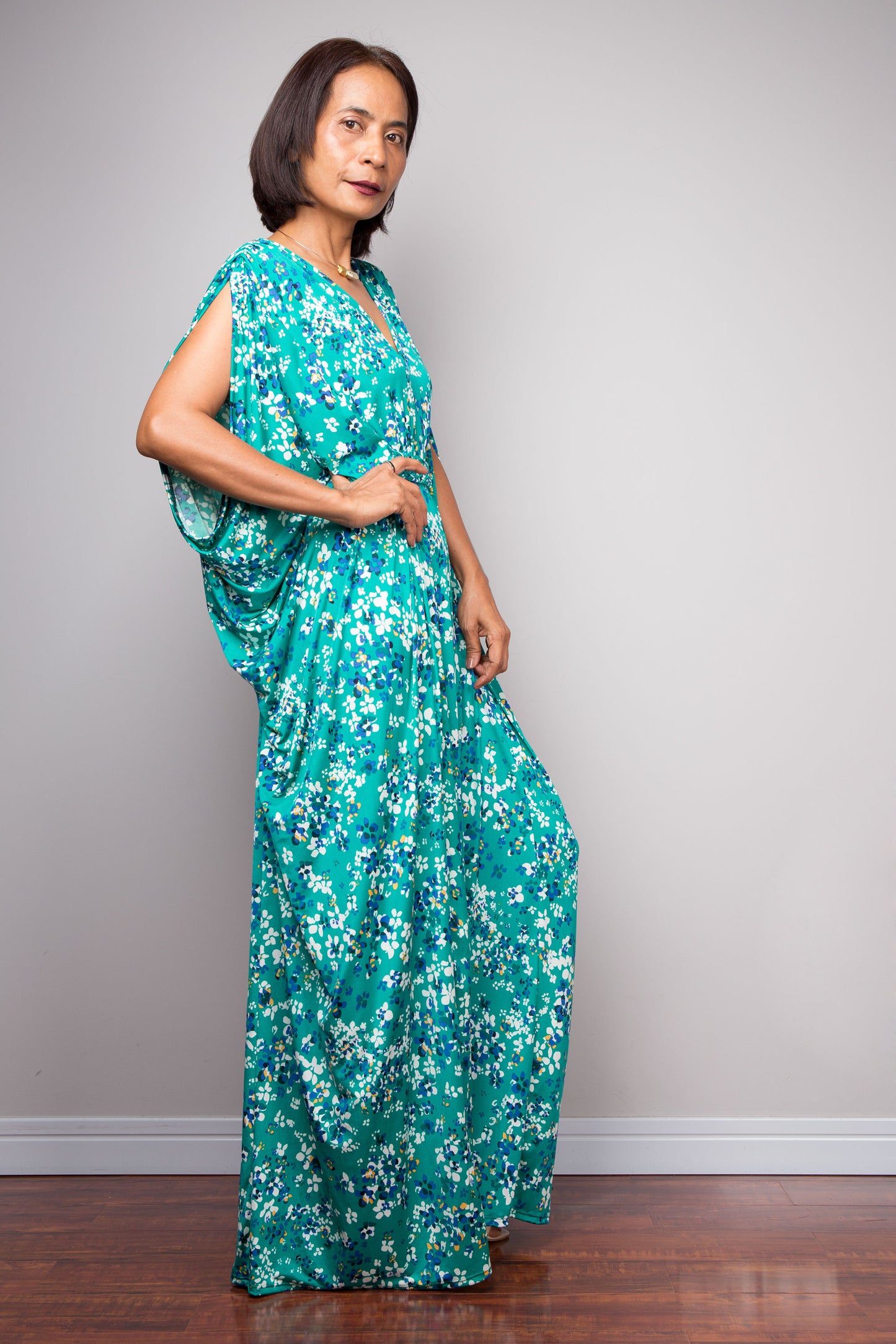 Woman wearing a teal floral maxi dress against a plain background