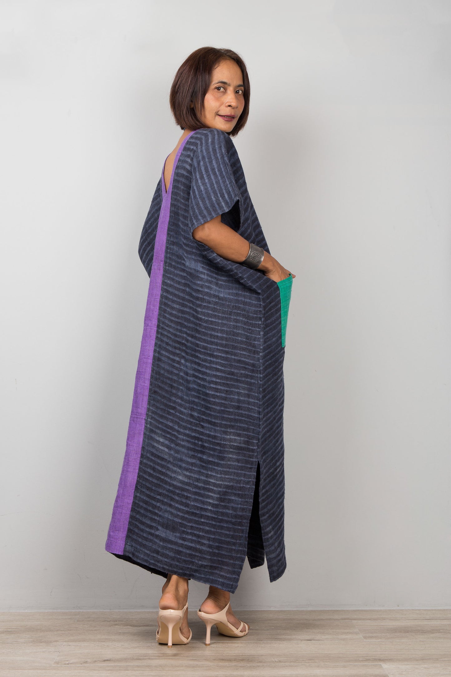 Woman wearing a long, dark blue dress with a purple stripe on a plain background