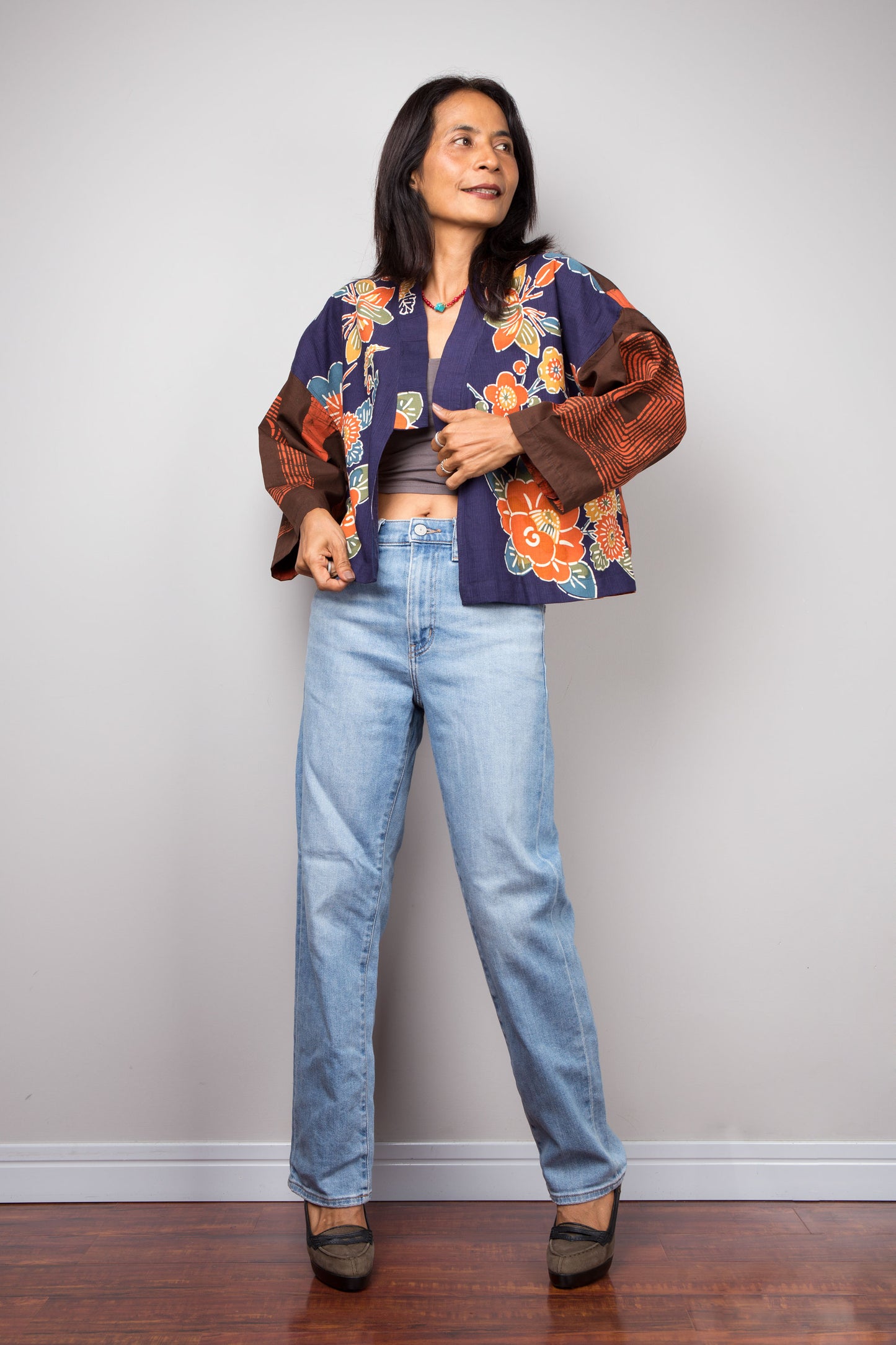 Woman wearing a floral kimono jacket and blue jeans against a plain background