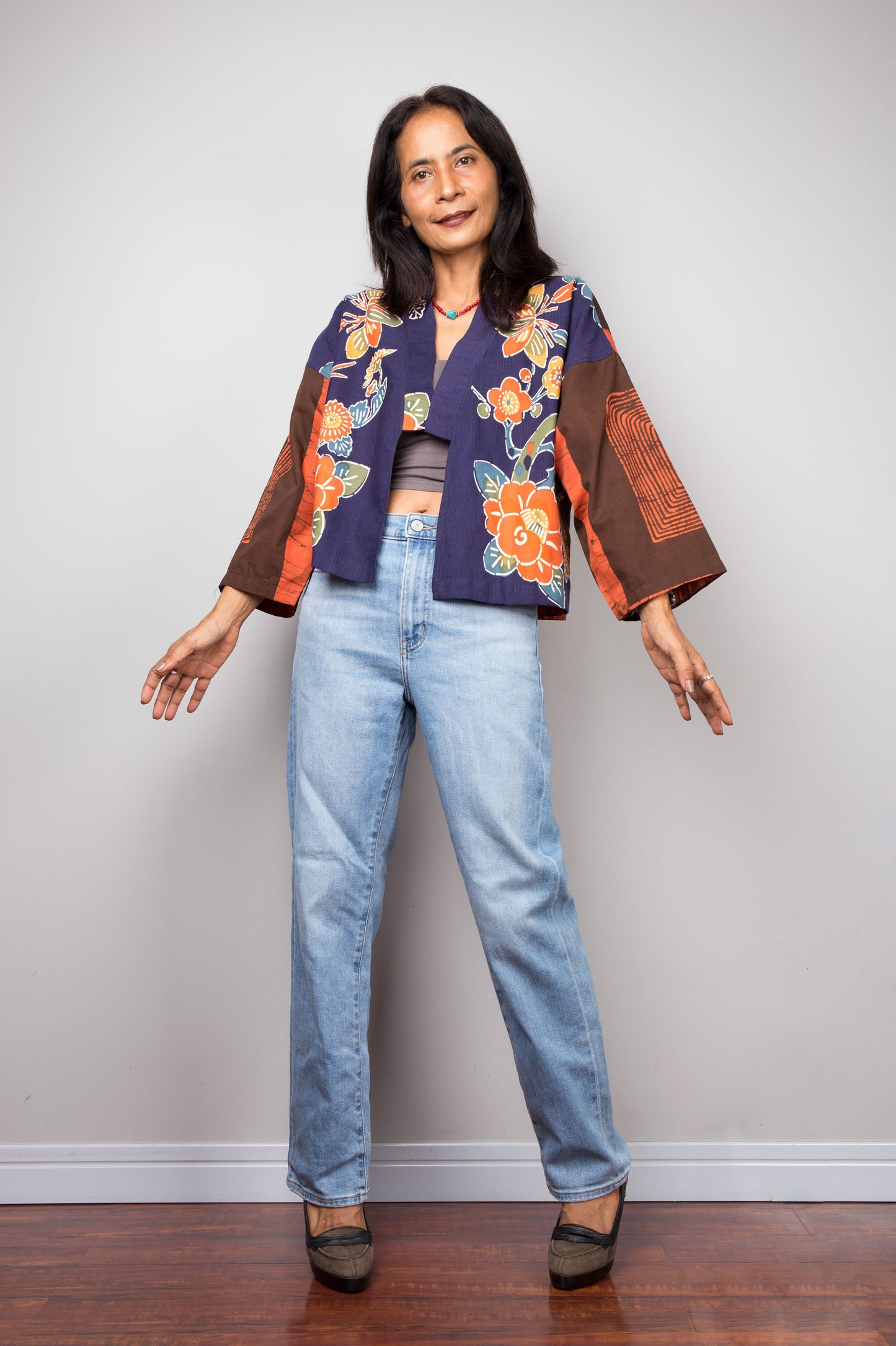 Woman wearing a floral kimono jacket by Nuichan and jeans against a plain background