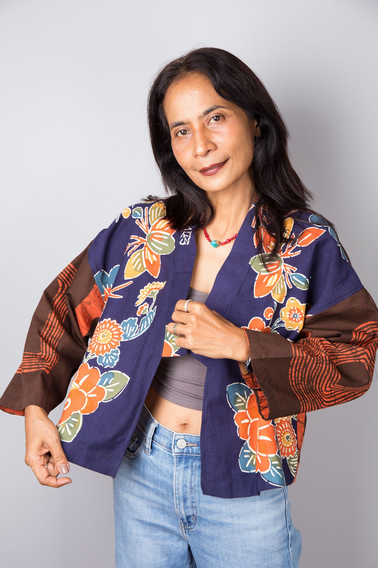 Woman wearing a colorful floral kimono jacket over a gray top and blue jeans on a plain background. Nuichan cotton kimono jacket design