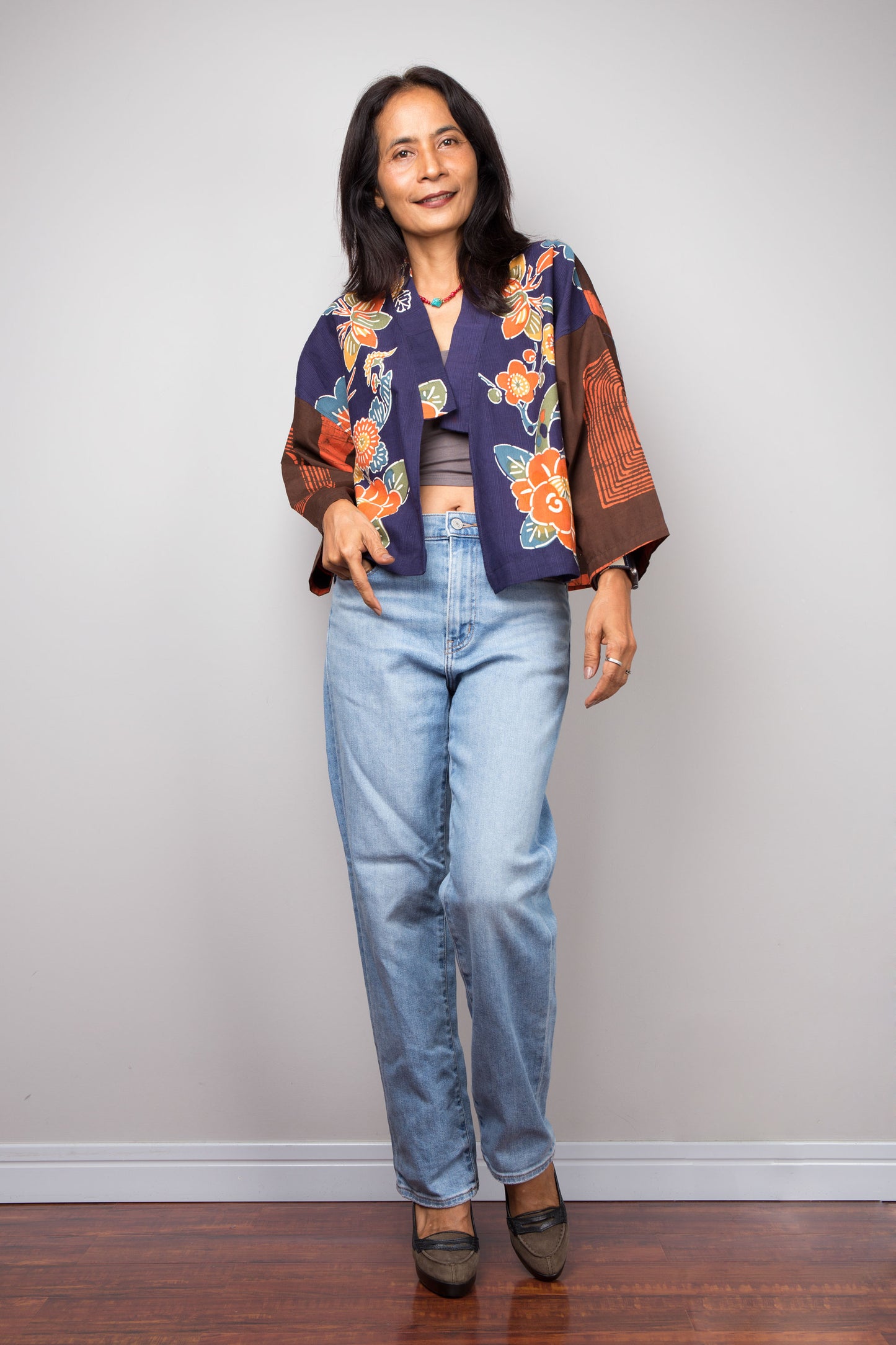 Woman wearing a colorful kimono jacket and jeans against a plain background