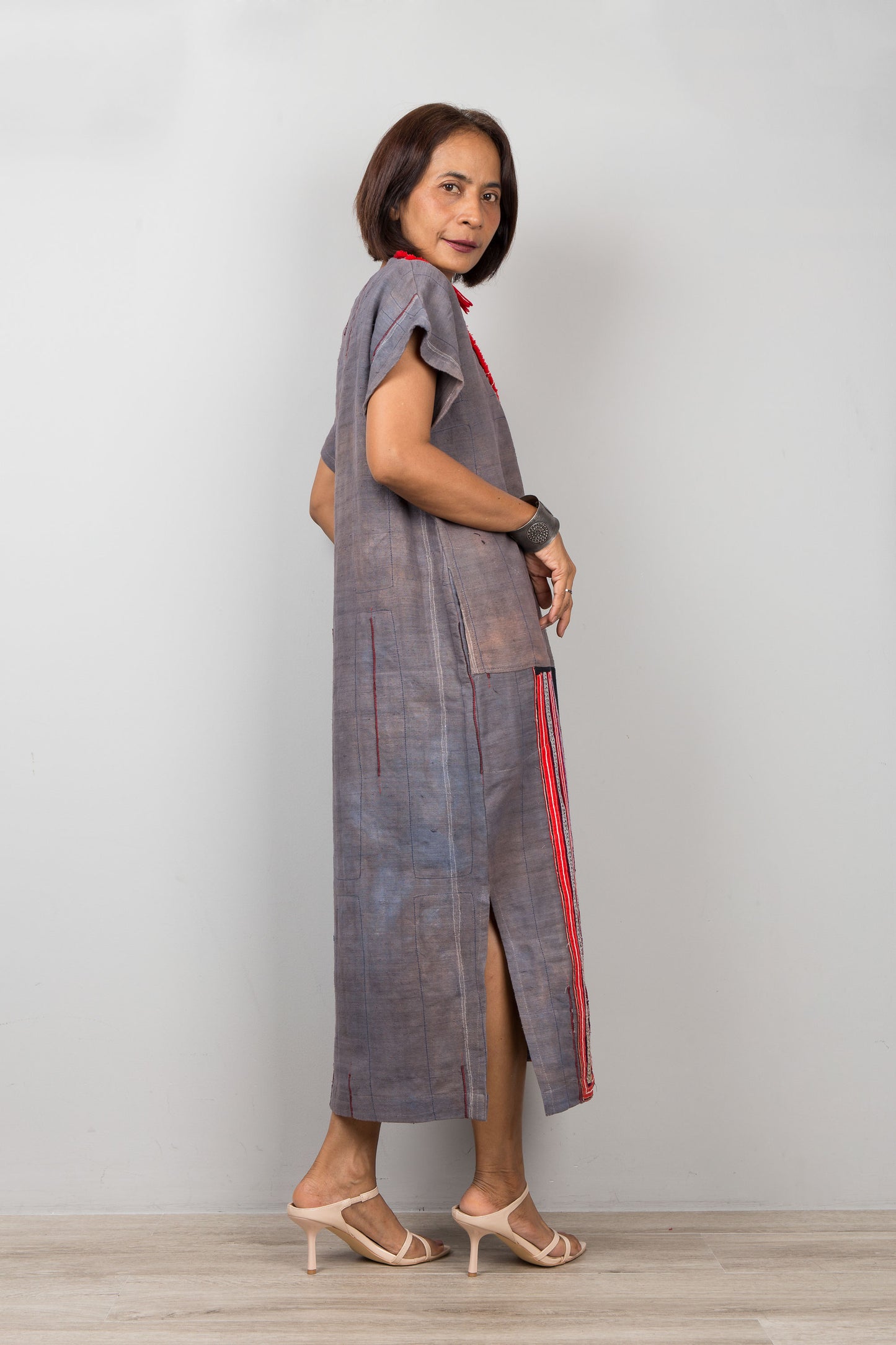 Woman wearing grey , short sleeve, kaftan with side splits and with traditional embroidery on the bottom part of the dress