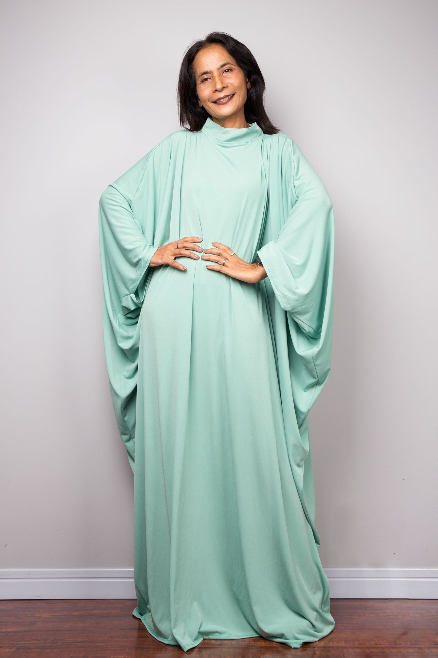 Woman wearing a mint green caftan maxi dress against a plain background