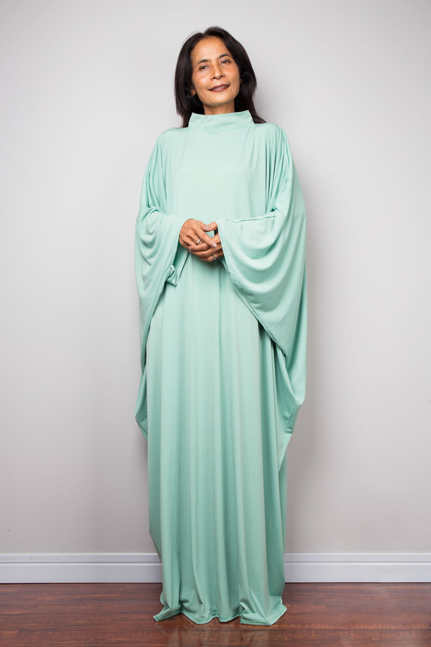 Woman wearing a light green caftan maxi dress against a plain background