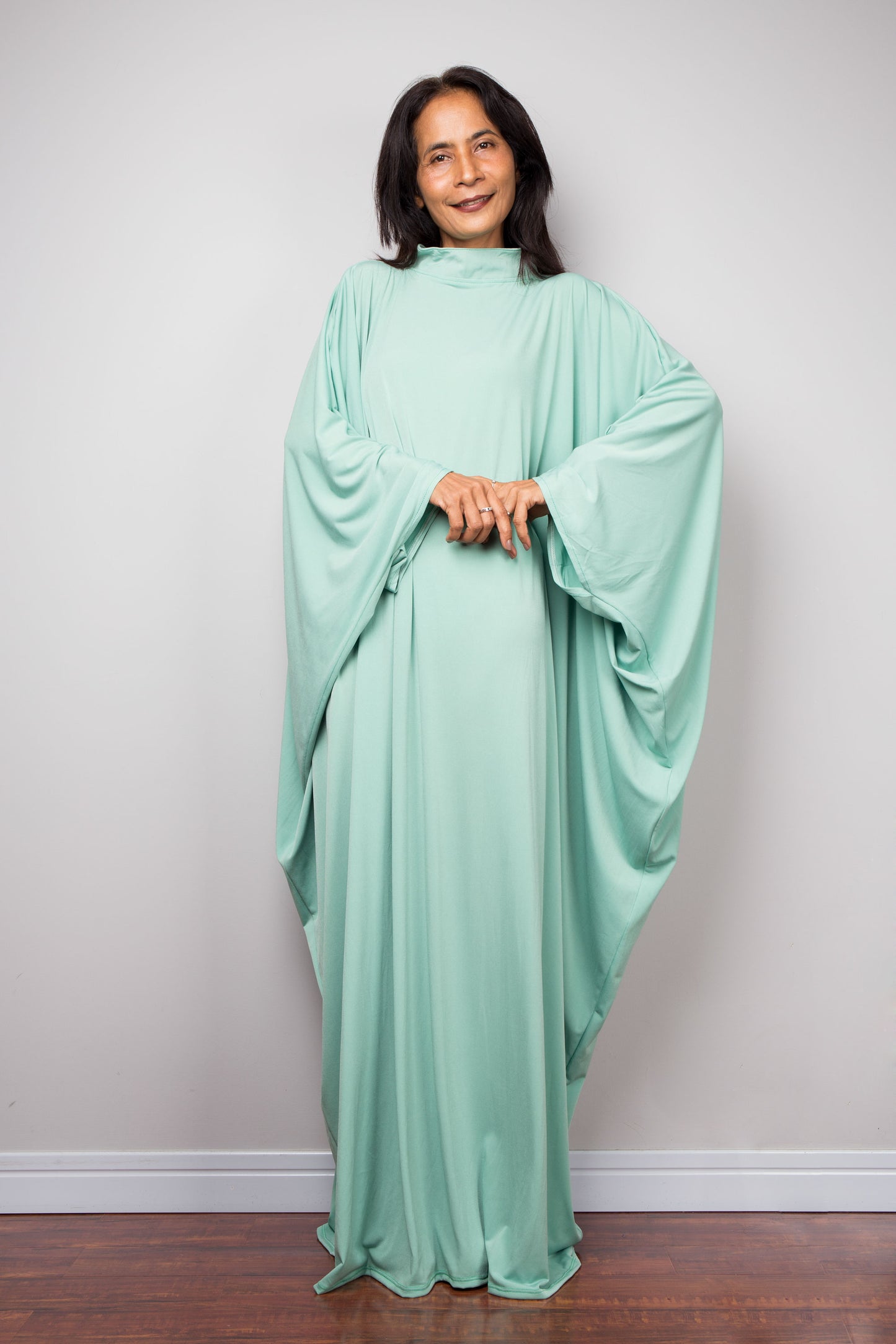 Woman wearing a light green kaftan maxi dress against a plain background
