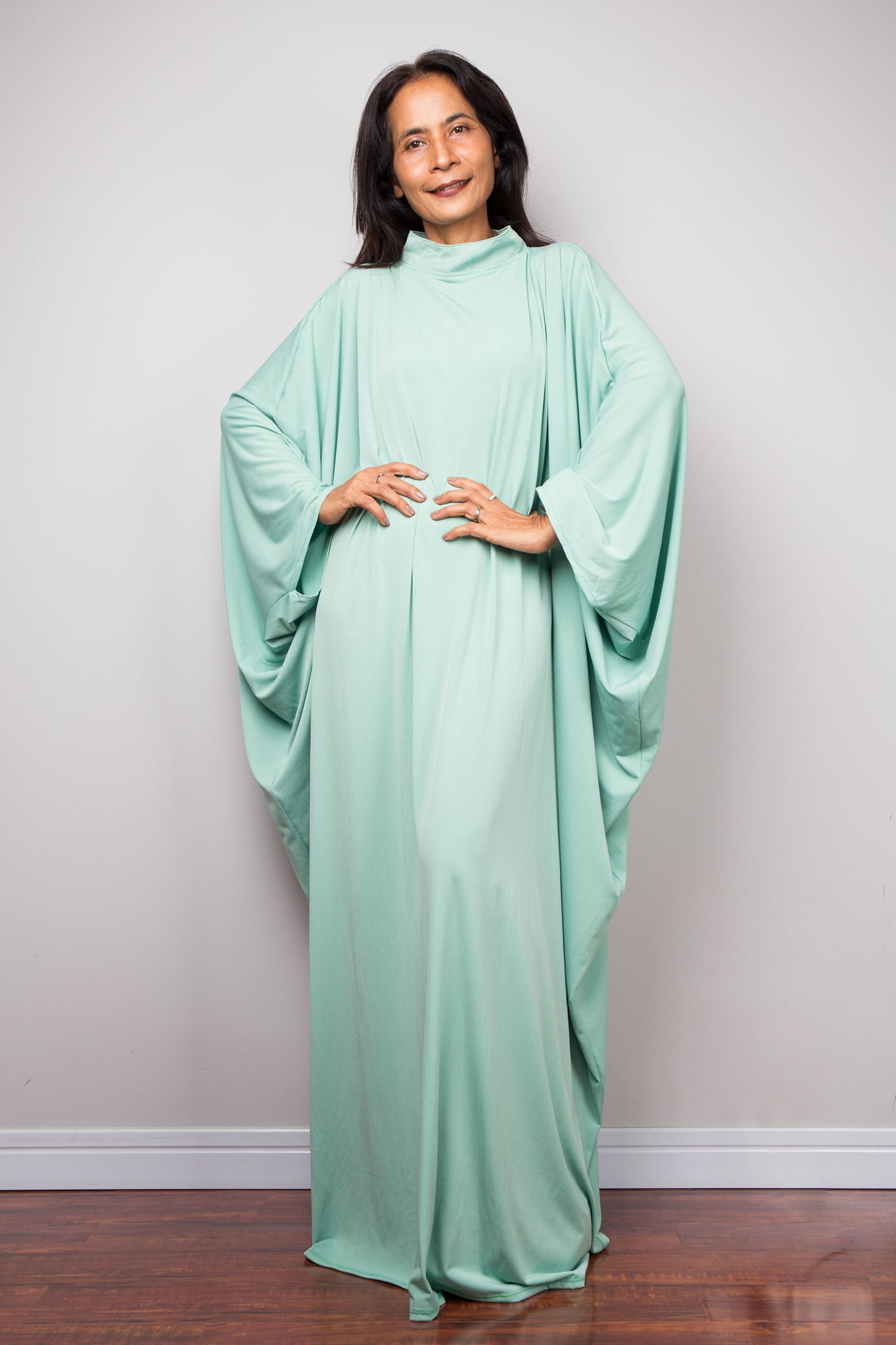 Woman wearing a mint green caftan dress against a plain background