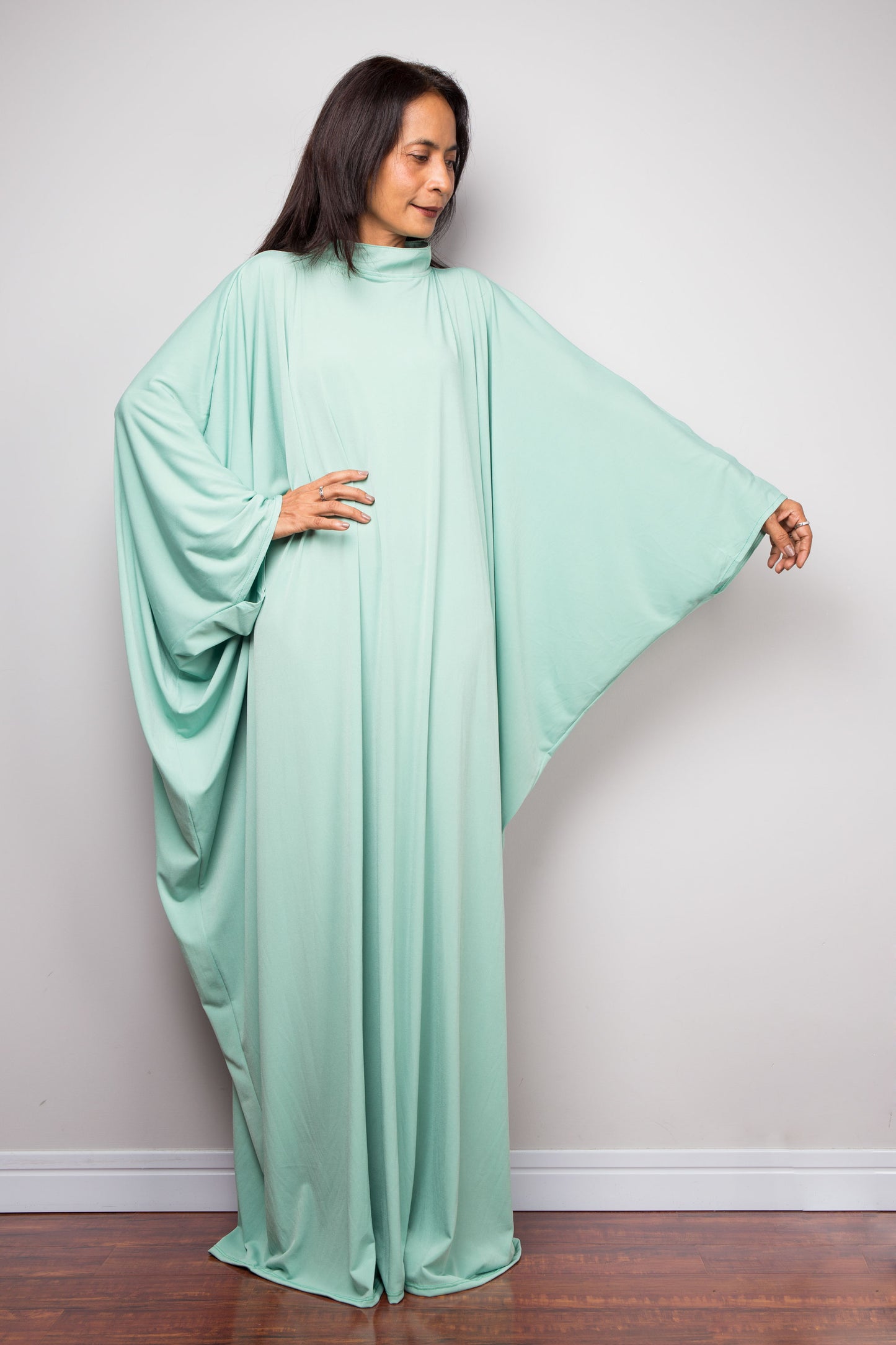 Woman wearing a mint green abaya caftan dress against a plain background
