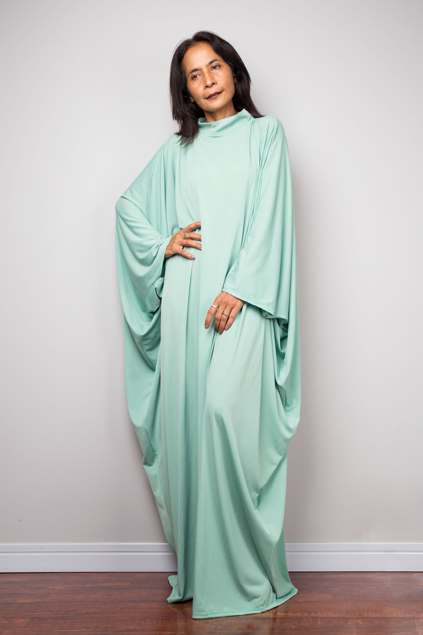 Woman wearing a mint green kaftan dress against a plain background