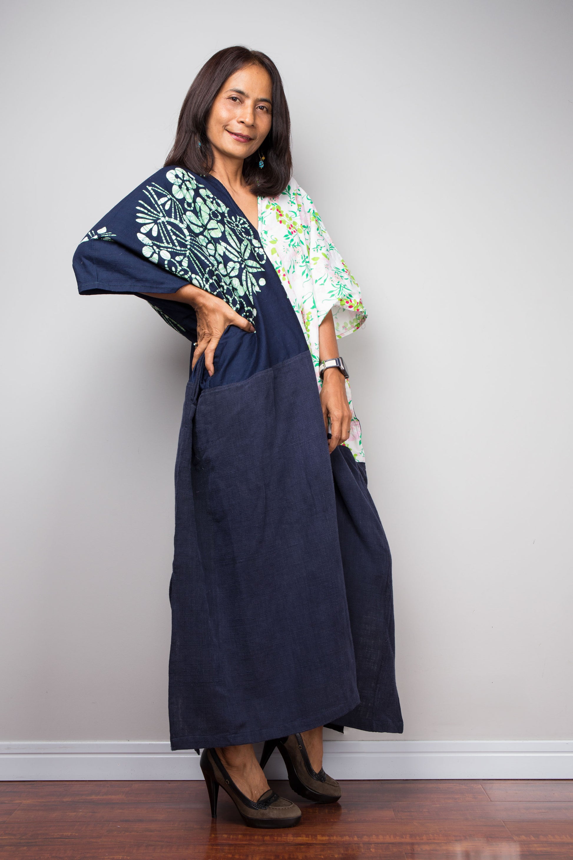 Woman wearing a navy blue dress with a floral patterned patches against a plain background