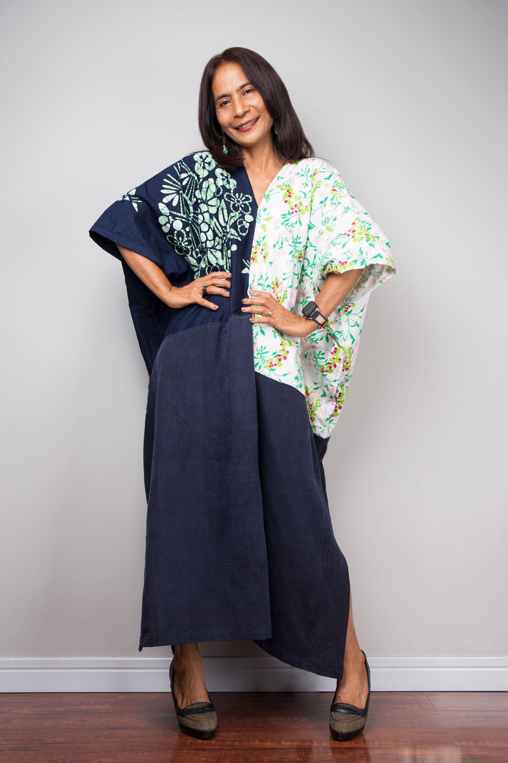 Woman wearing a long navy dress with floral patterns on a plain background