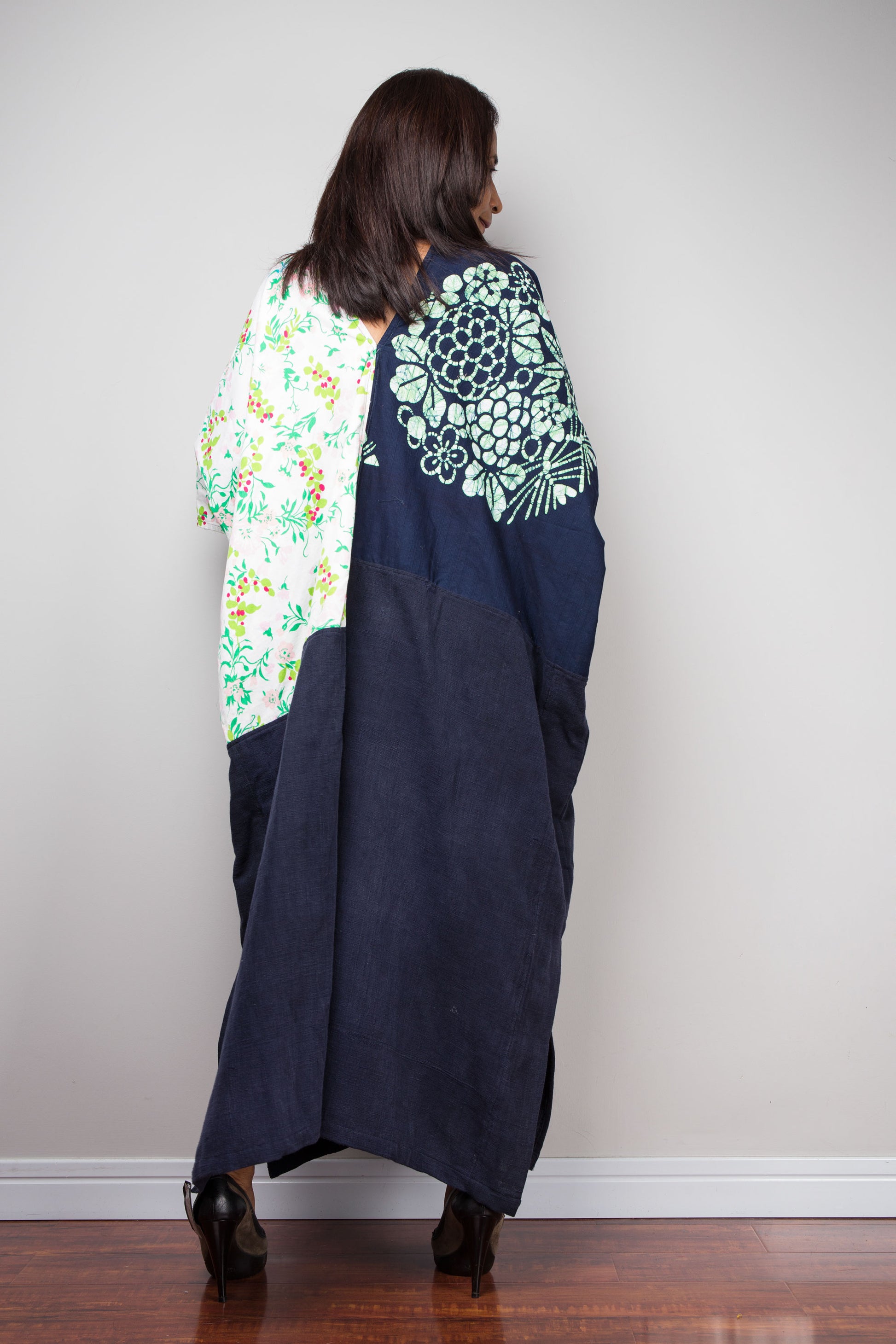 Woman wearing a long, dark blue kaftan with floral patterns on a plain background