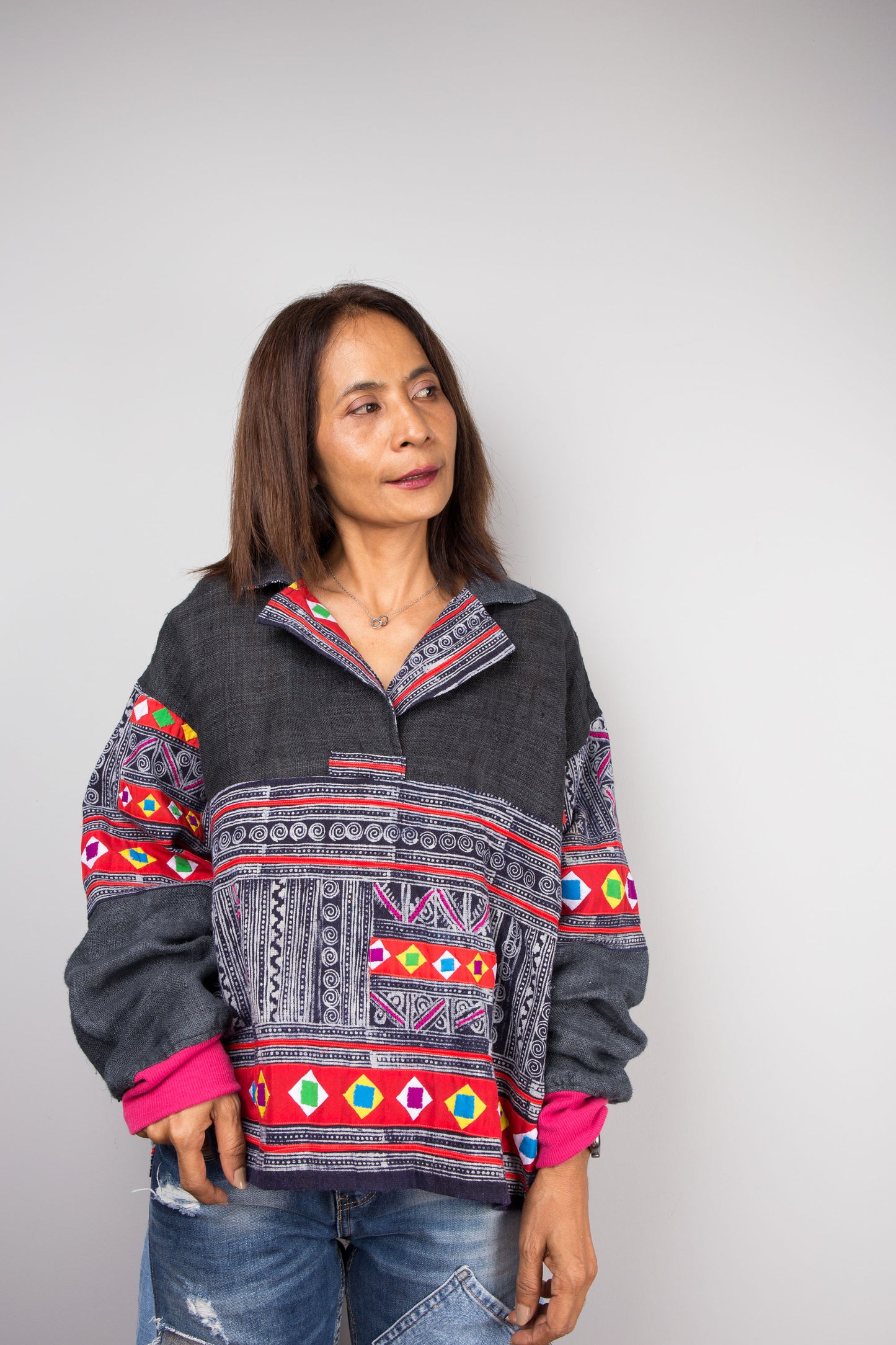 Dark grey hand-batik pullover tunic with batwing sleeves and patchwork by Nuichan on a woman, paired with distressed jeans, set against a gray wall