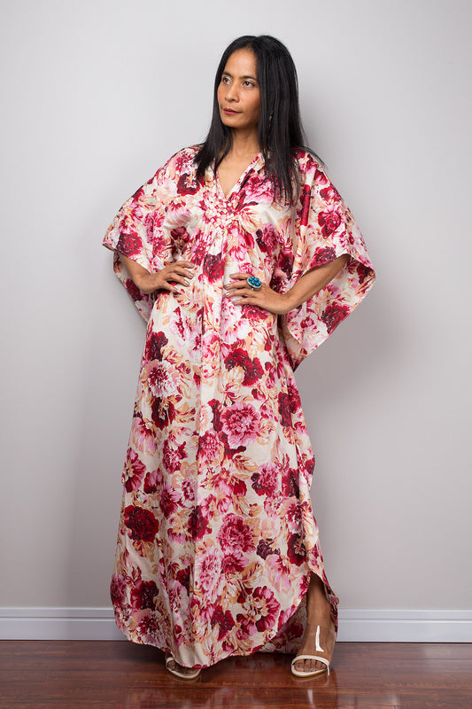 Woman wearing a pink floral caftan dress against a plain background