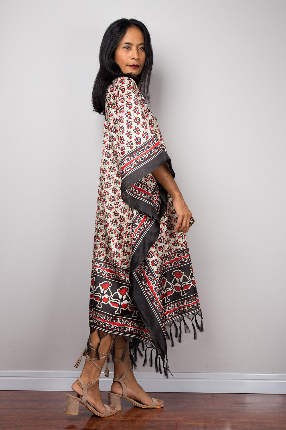 Woman wearing a patterned caftan tunic dress with fringe on a plain background