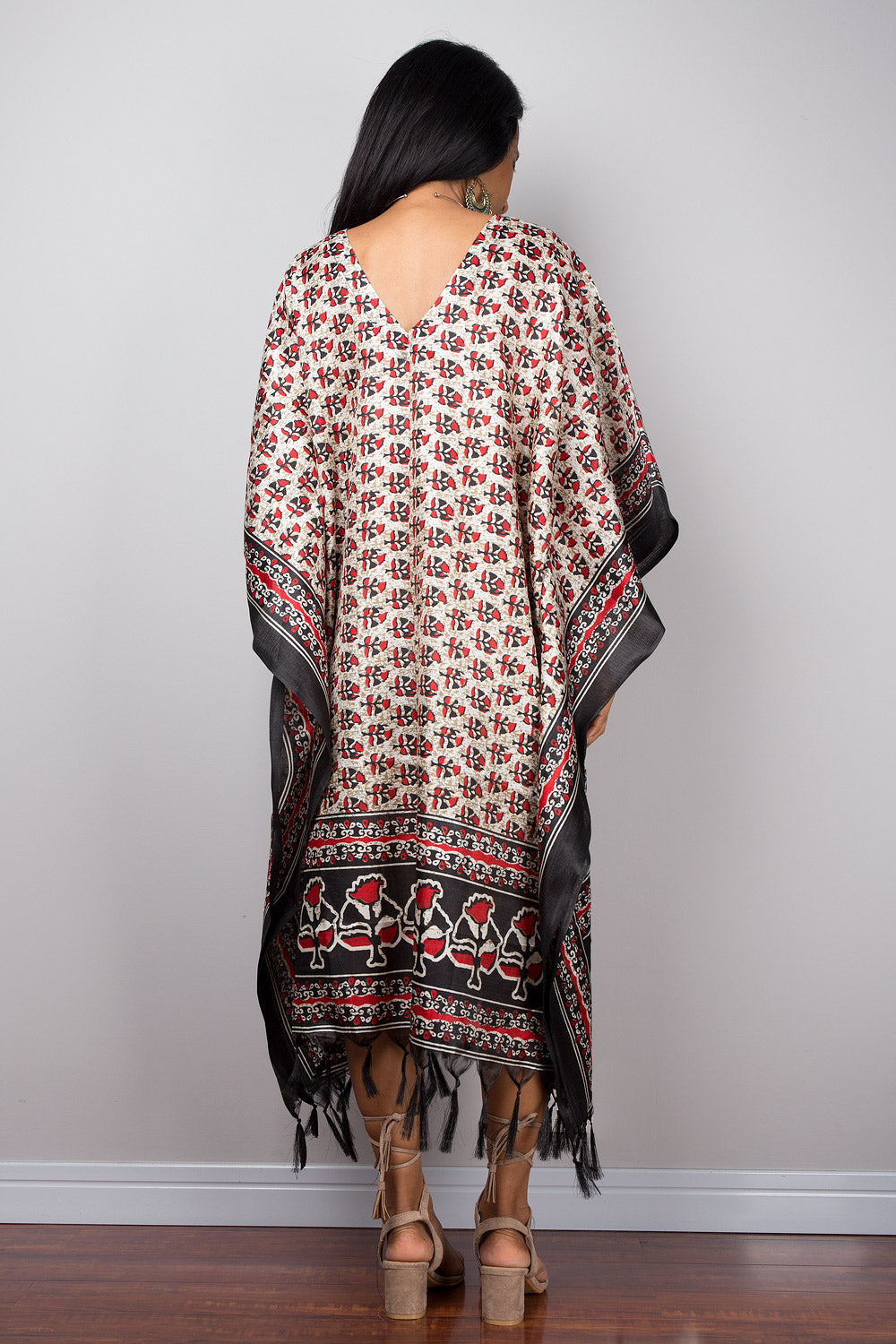 Woman wearing a patterned caftan tunic dress with fringe against a plain background