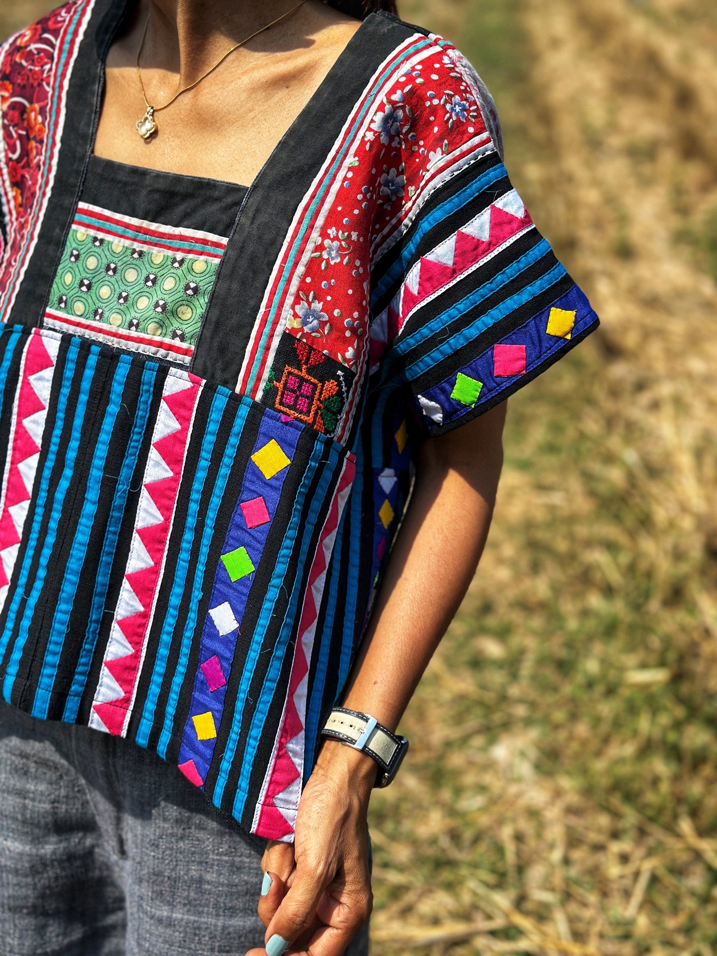 Nuichan’s multicolor Hmong tribal crop top with black, blue, magenta, and red stripes, worn by a woman with dark hair. Close up front part